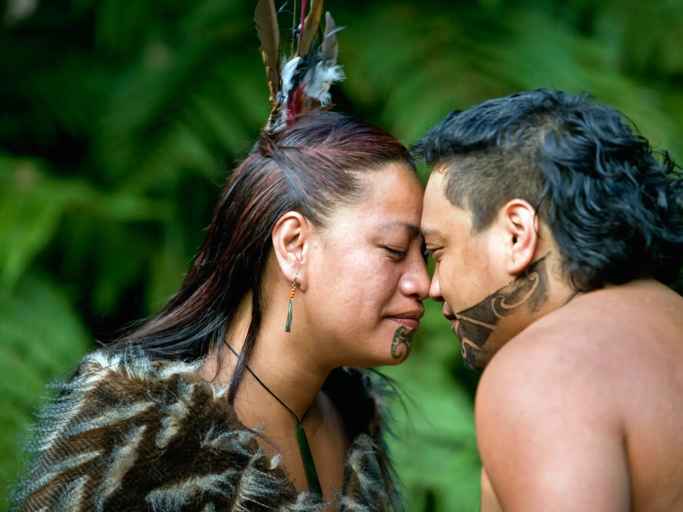 Maori-Mann und -Frau mit traditionellen Tā Moko-Tattoos praktizieren die Hongi-Begrüßung Stirn an Stirn in Neuseeland.