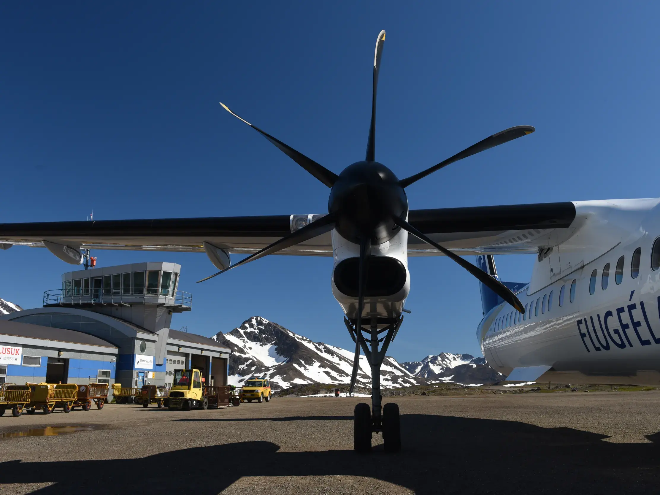 Propellerflugzeug am Flughafen von Kulusuk in Ostgrönland, im Hintergrund erheben sich schneebedeckte Berge.