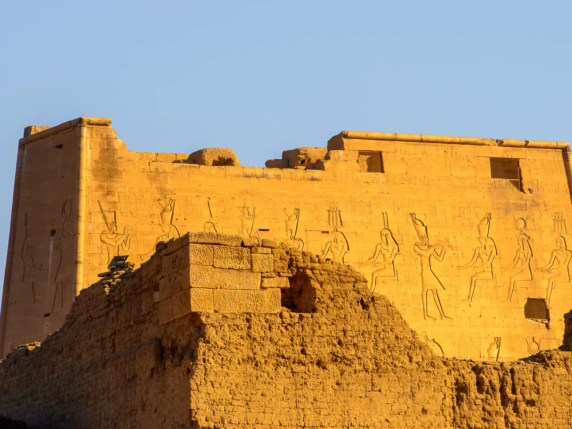 Außenfassade des Horus-Tempels in Edfu mit altägyptischen Reliefs an der Pylonwand unter strahlend blauem Himmel.