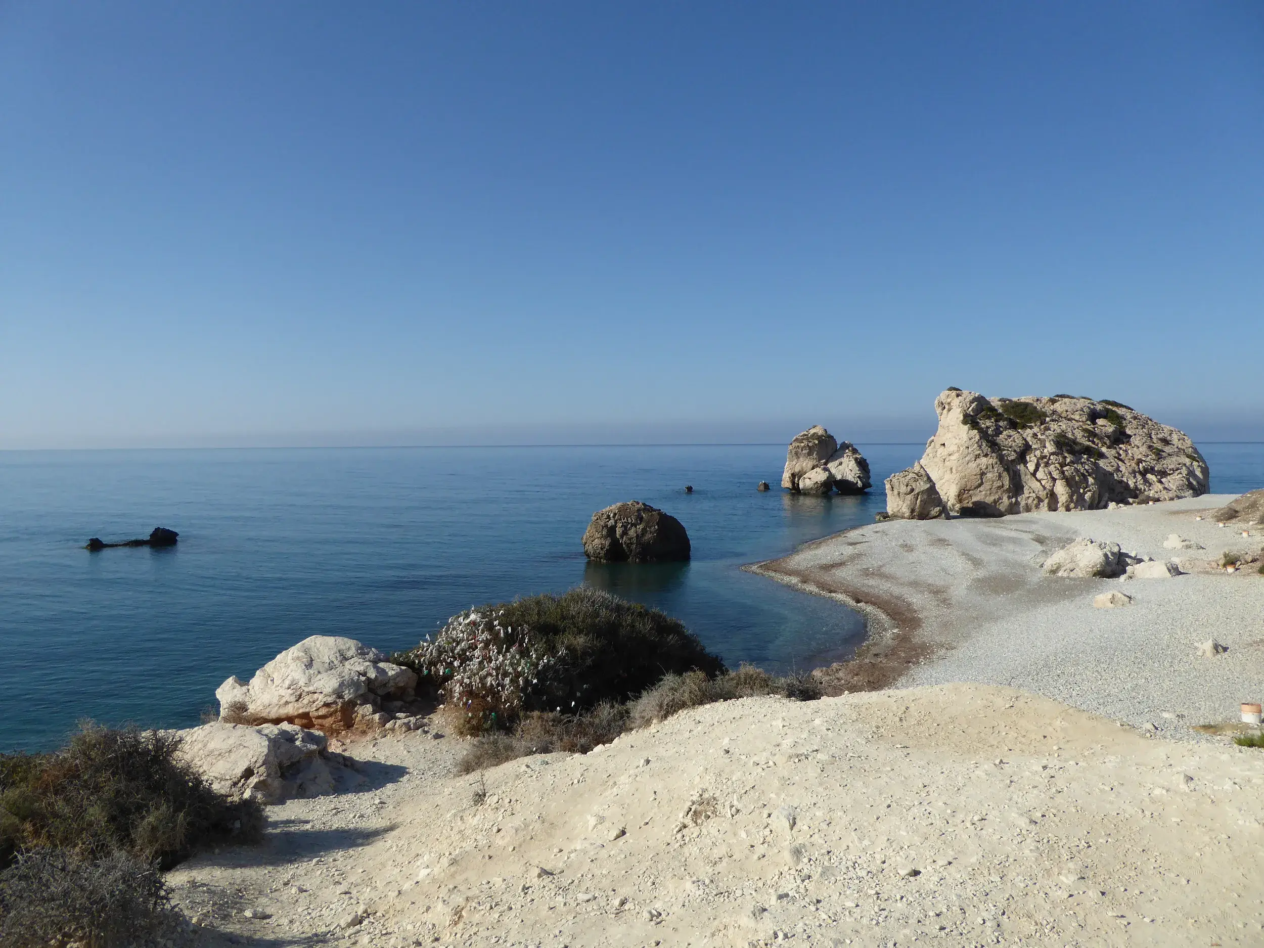 Sonniger Blick auf den Kieselstrand und die Felsen der Aphrodite, Petra tou Romiou, im blauen Mittelmeer vor der Küste Zyperns.