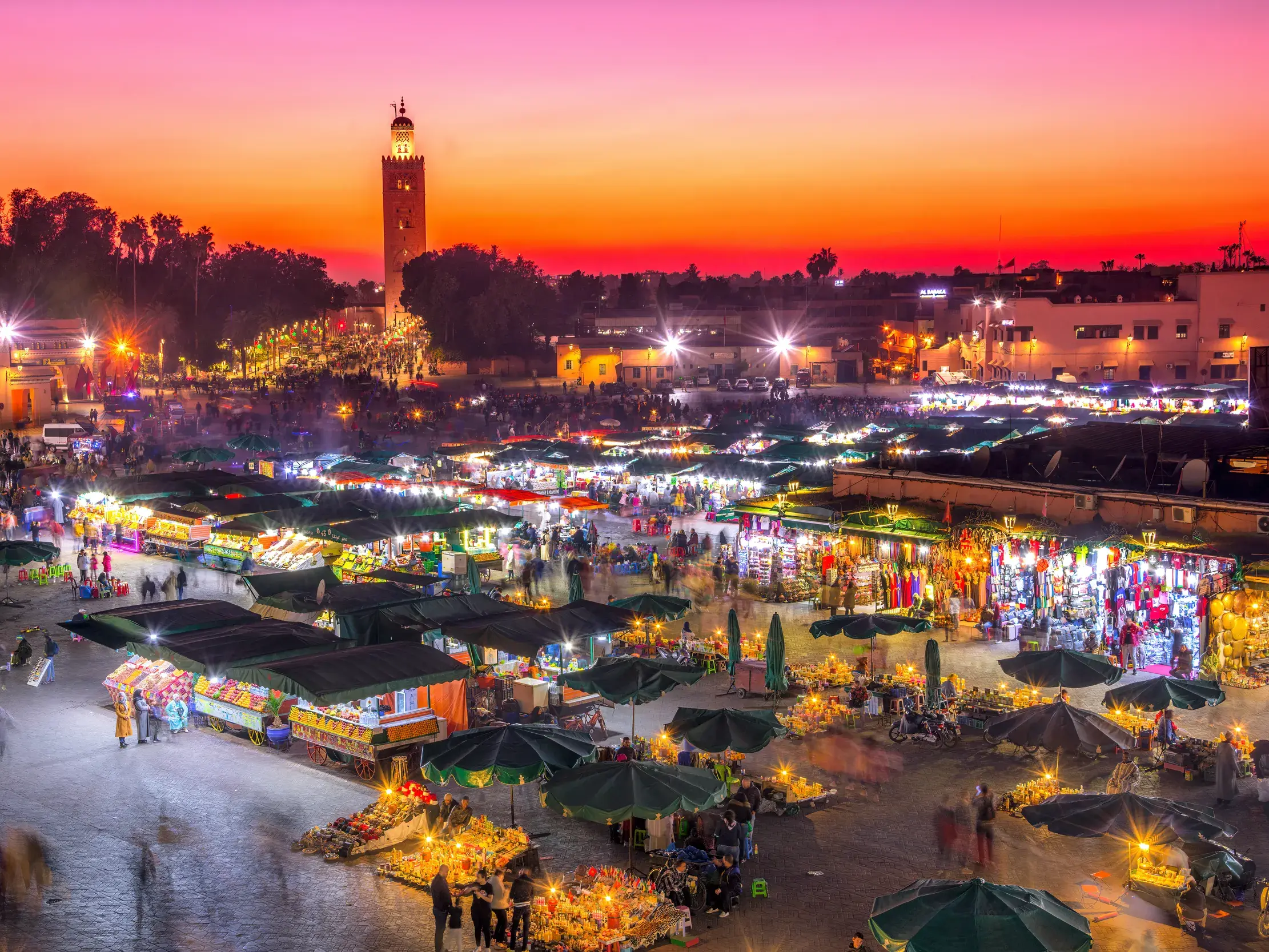 Lebhaftes Treiben auf dem Djemaa el Fna in Marrakesch. Bei Dämmerung leuchten die Marktstände vor der Kulisse der Koutoubia-Moschee.