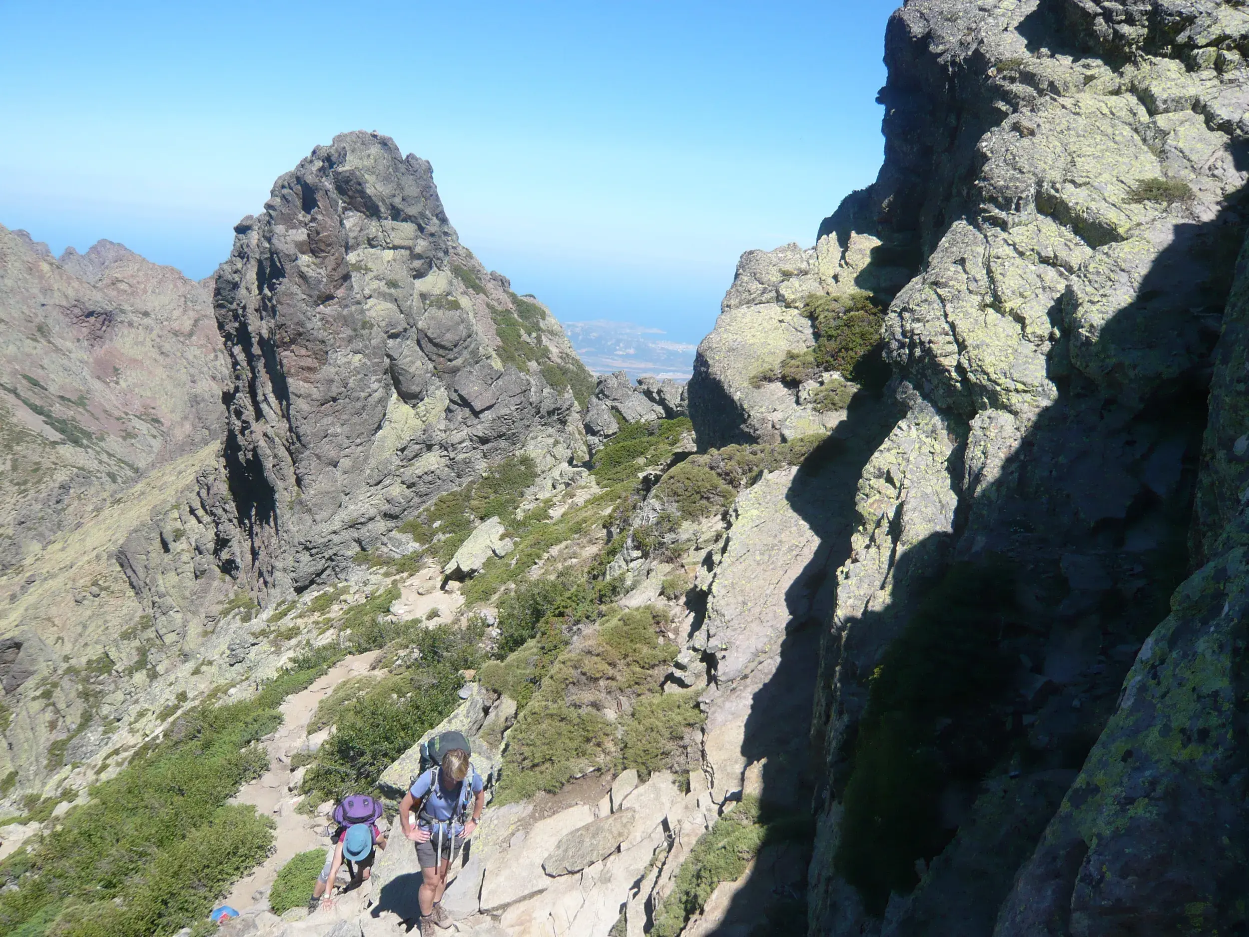 Zwei Wanderer mit Rucksäcken auf dem anspruchsvollen GR 20 auf Korsika, umgeben von schroffen Granitfelsen.
