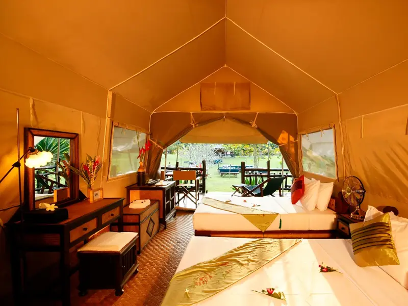 Innenansicht eines luxuriösen Zeltes im Hintok River Camp am River Kwai mit zwei Betten, Möbeln und Blick ins Grüne.
