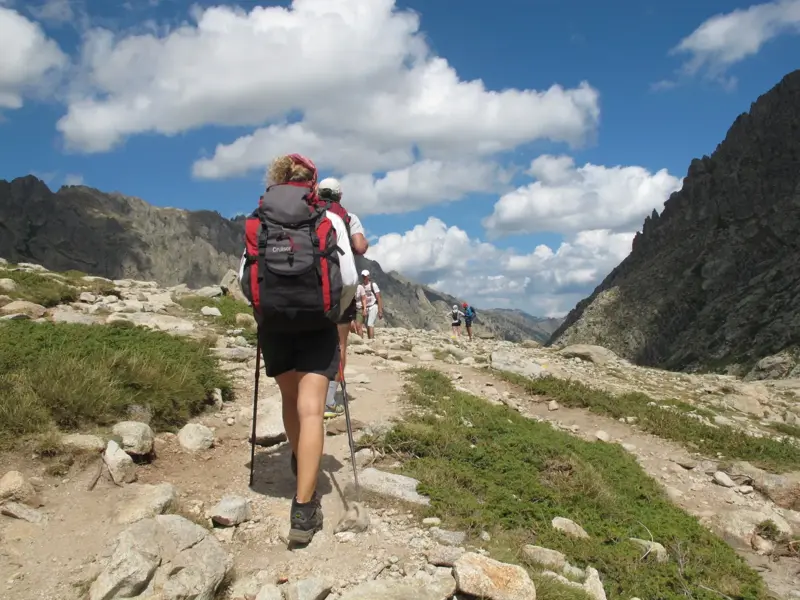 Wandergruppe mit Rucksäcken beim Trekking auf dem steinigen Fernwanderweg GR20 in der felsigen Bergwelt Korsikas.