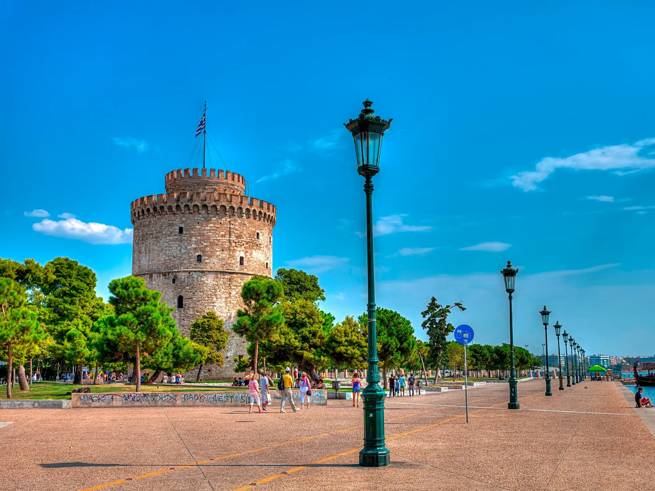 Der Weiße Turm, das Wahrzeichen von Thessaloniki, an der sonnigen Hafenpromenade mit Spaziergängern am Meer.
