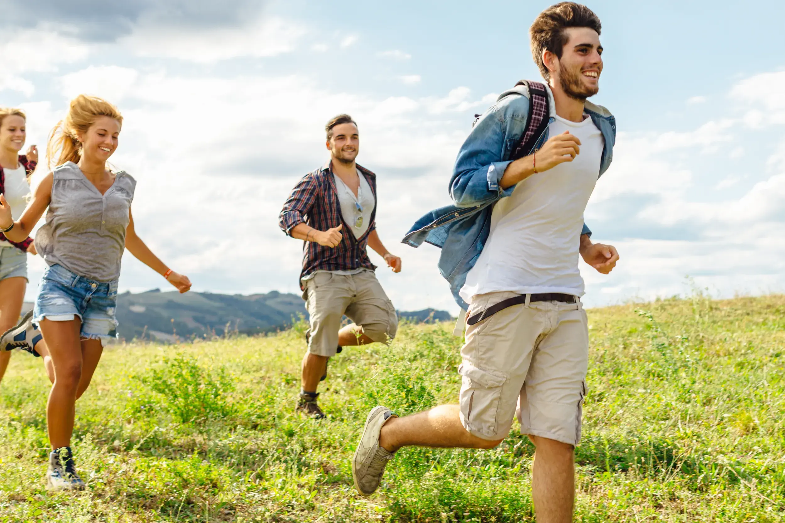 Eine junge Reisegruppe läuft gut gelaunt während einer Highland-Wanderung durch die weite, grüne Landschaft Schottlands.