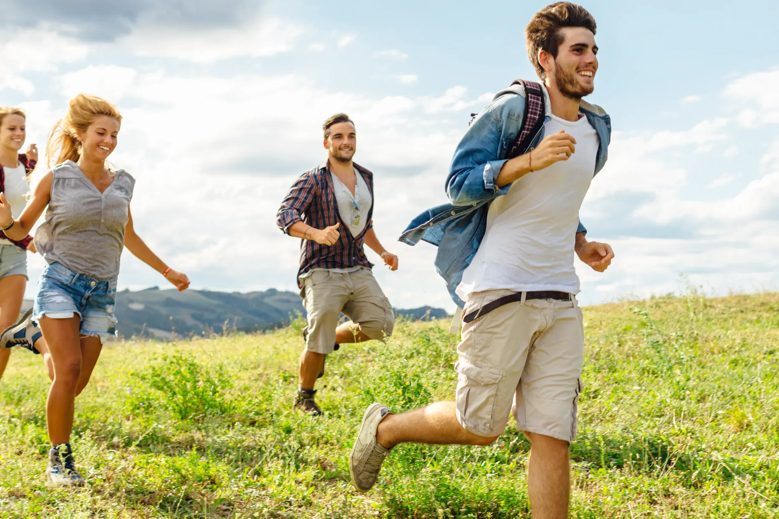 Eine junge Reisegruppe läuft gut gelaunt während einer Highland-Wanderung durch die weite, grüne Landschaft Schottlands.