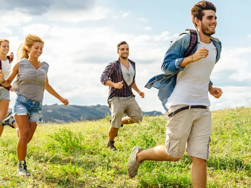 Eine junge Reisegruppe läuft gut gelaunt während einer Highland-Wanderung durch die weite, grüne Landschaft Schottlands.