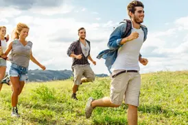 Eine junge Reisegruppe läuft gut gelaunt während einer Highland-Wanderung durch die weite, grüne Landschaft Schottlands.