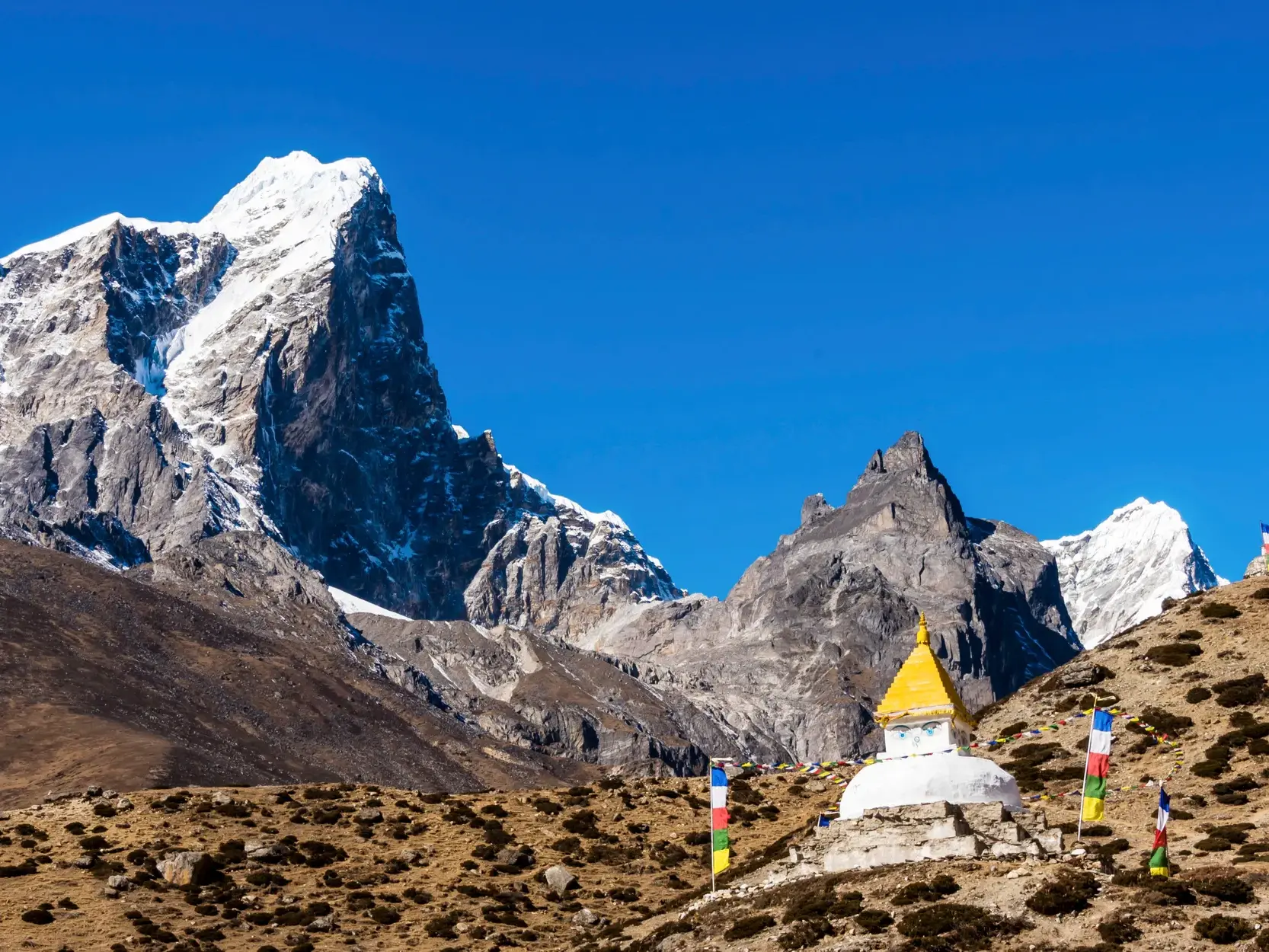 Trekking im Khumbu-Gebiet: Ein weißer Chörten mit Gebetsfahnen vor der Kulisse eines schneebedeckten Himalaya-Gipfels.