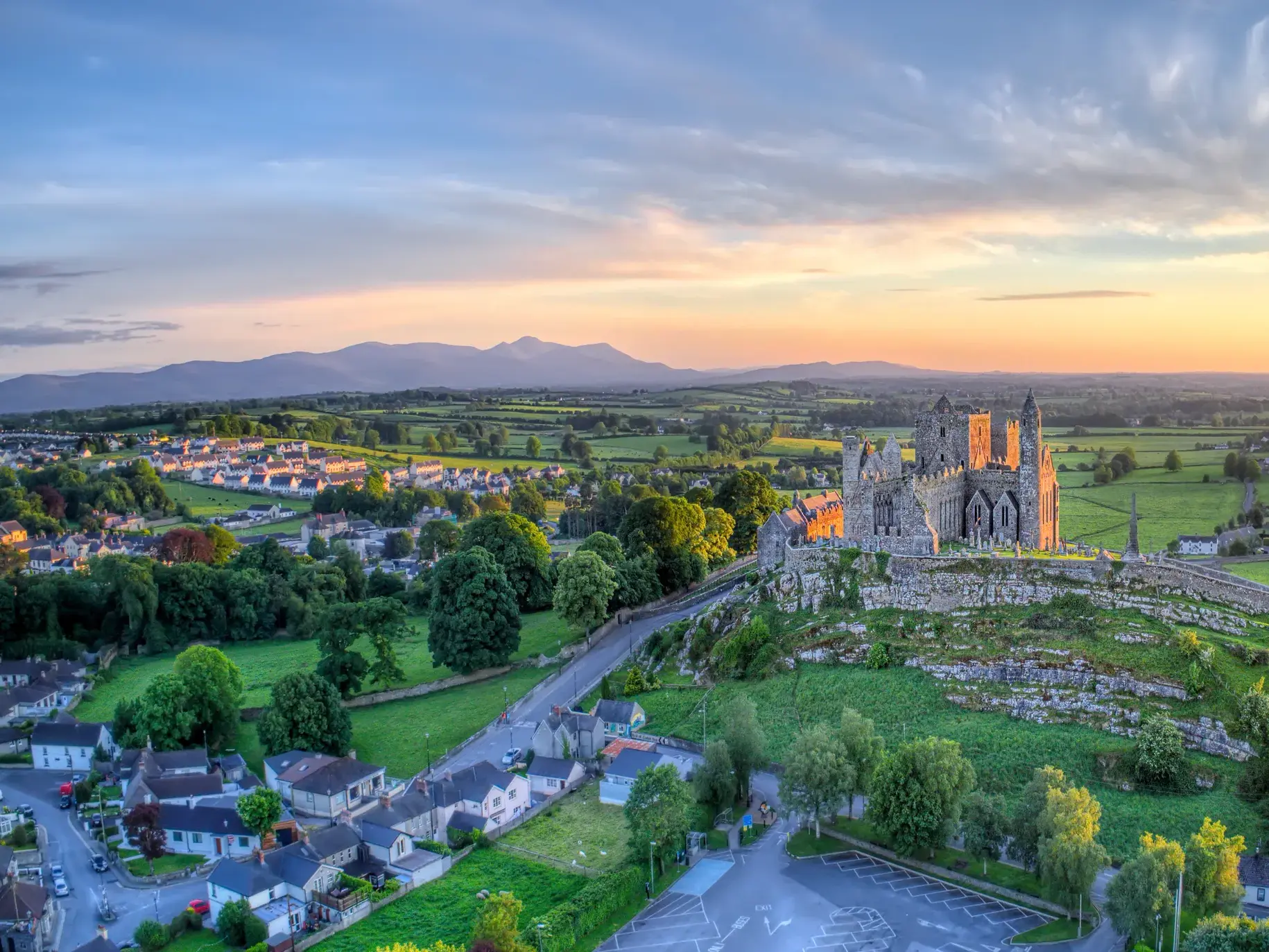 Der Rock of Cashel, die irische Akropolis, thront bei Sonnenuntergang über der weiten, grünen Landschaft Irlands.