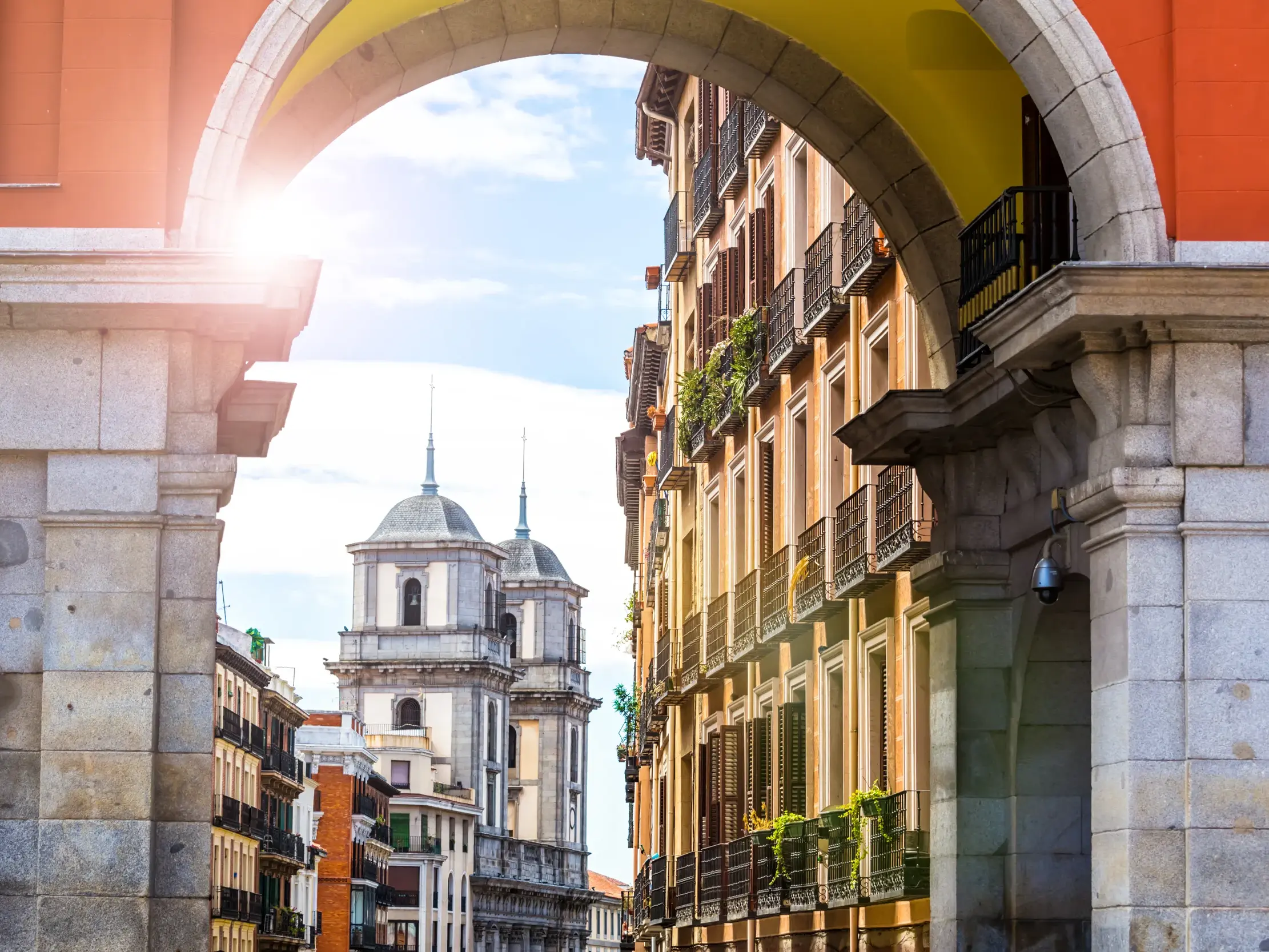 Ein steinerner Torbogen auf der herrschaftlichen Plaza Mayor in Madrid rahmt den Blick auf historische Häuser und Kirchtürme.