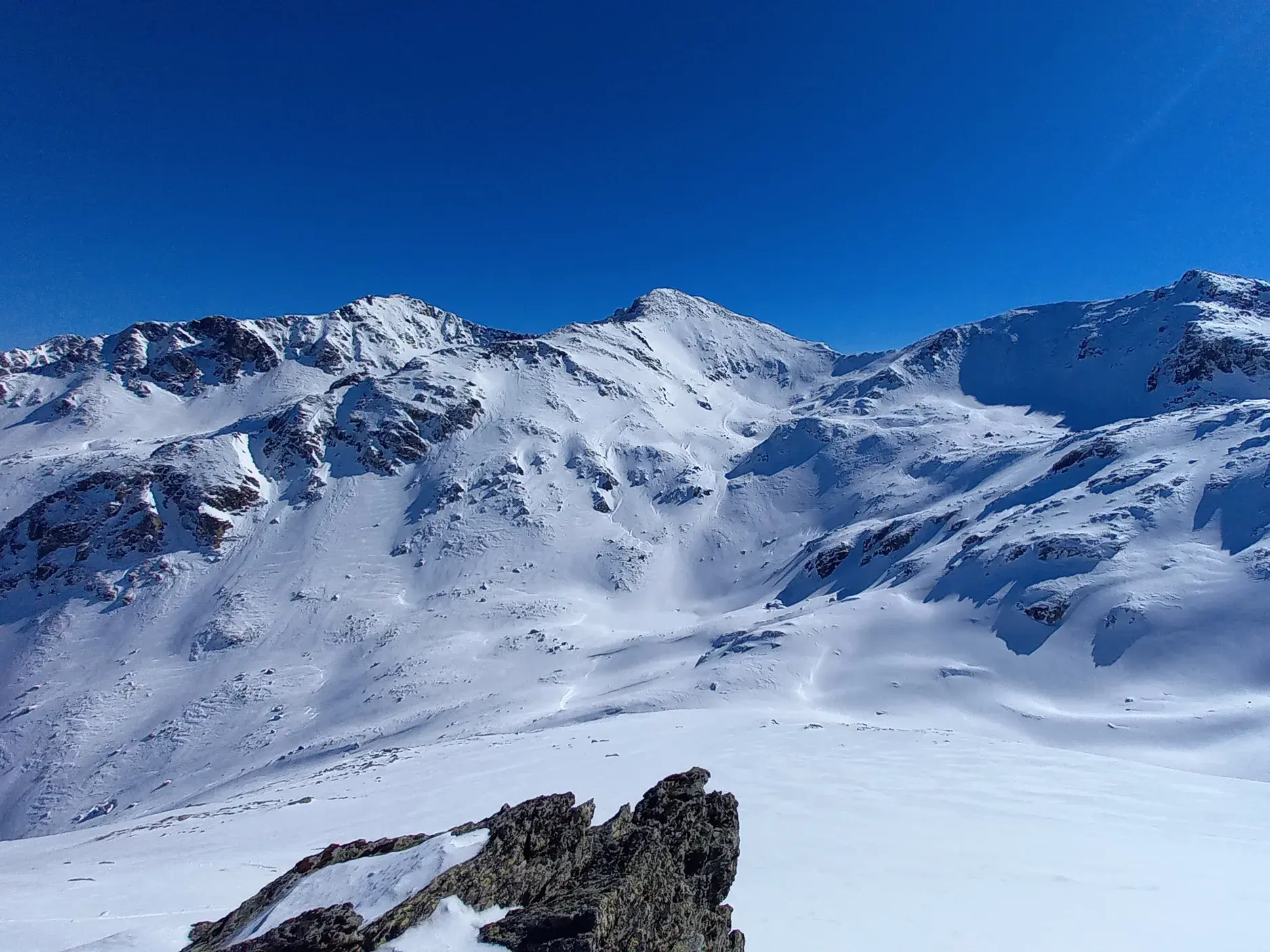 Panoramablick vom Gipfel auf die unberührte, weite Schneelandschaft des Korab-Gebirges unter strahlend blauem Himmel.