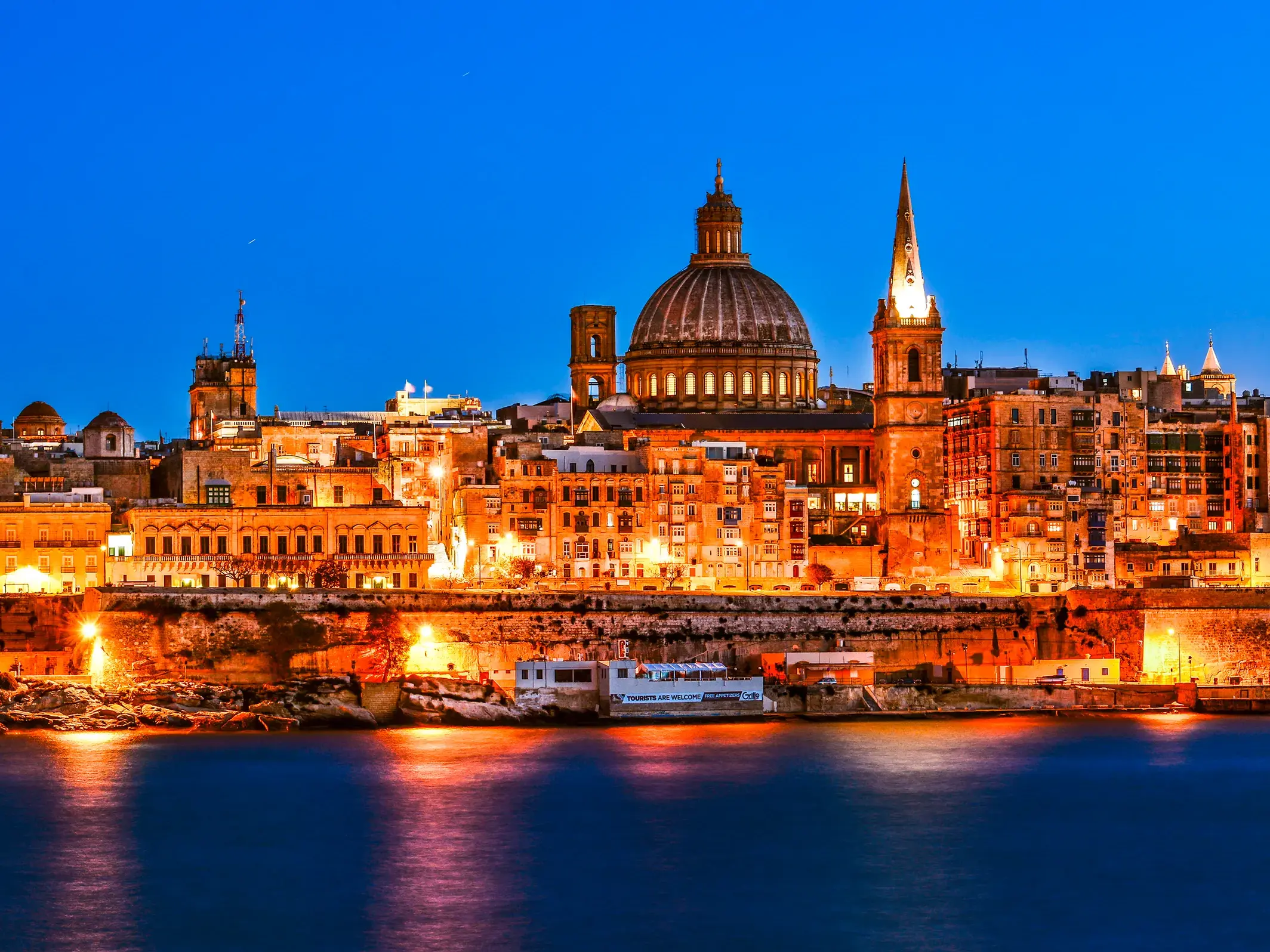 Die historische Skyline der UNESCO-Stadt Valletta auf Malta, eindrucksvoll beleuchtet bei blauer Stunde und vom Meer aus betrachtet.