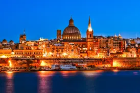 Die historische Skyline der UNESCO-Stadt Valletta auf Malta, eindrucksvoll beleuchtet bei blauer Stunde und vom Meer aus betrachtet.