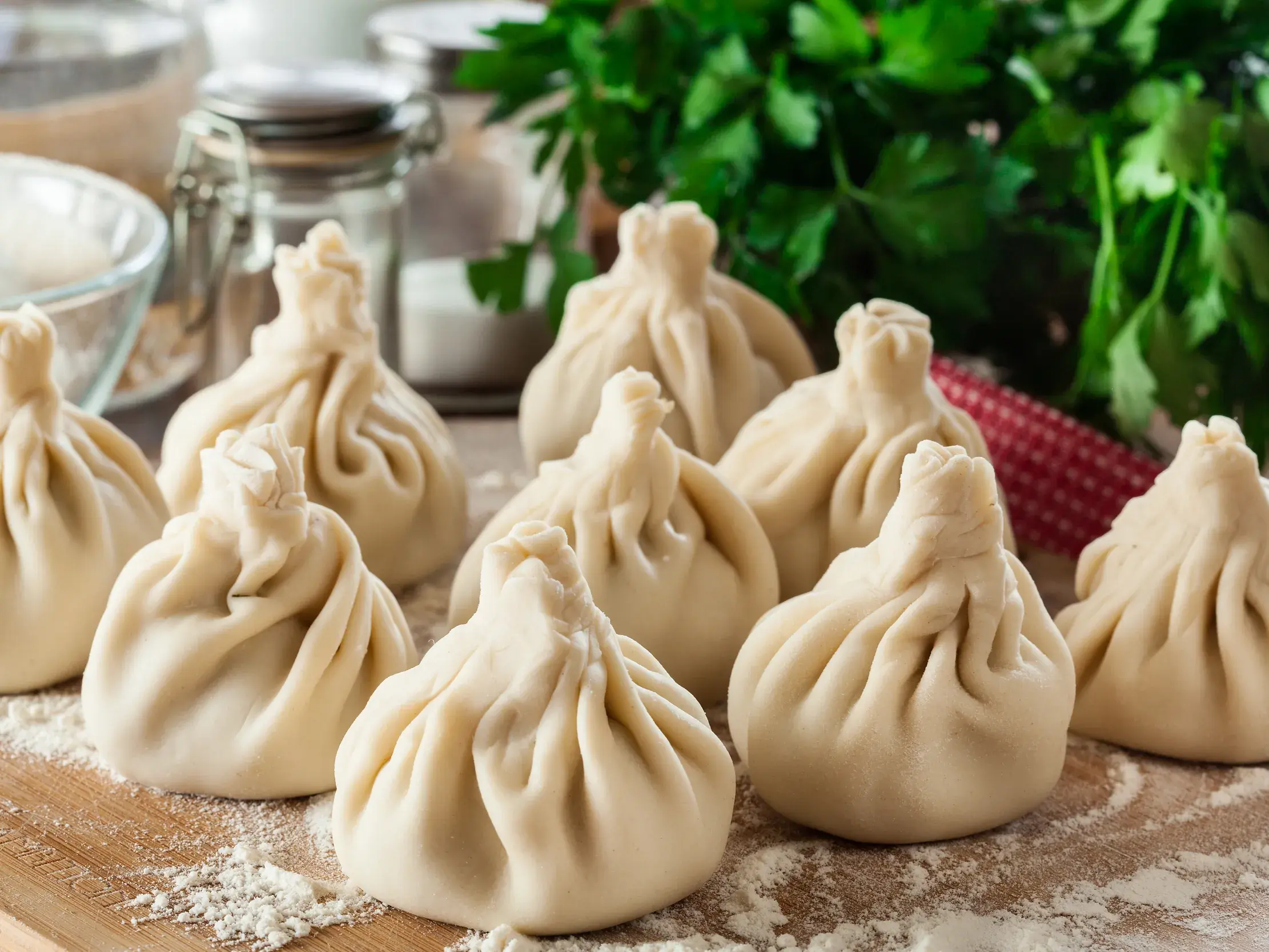Nahaufnahme von traditionellen georgischen Chinkali, frisch zubereitet auf einem Holzbrett mit Mehl und Kräutern.
