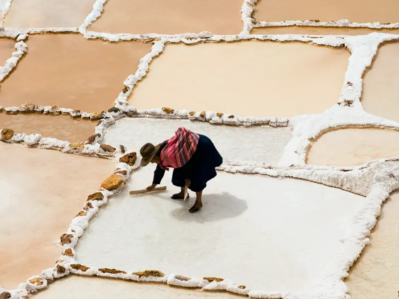 Eine Frau in traditioneller Kleidung bei der Salzernte in den terrassierten Salzbecken der Salinen von Maras in Peru.