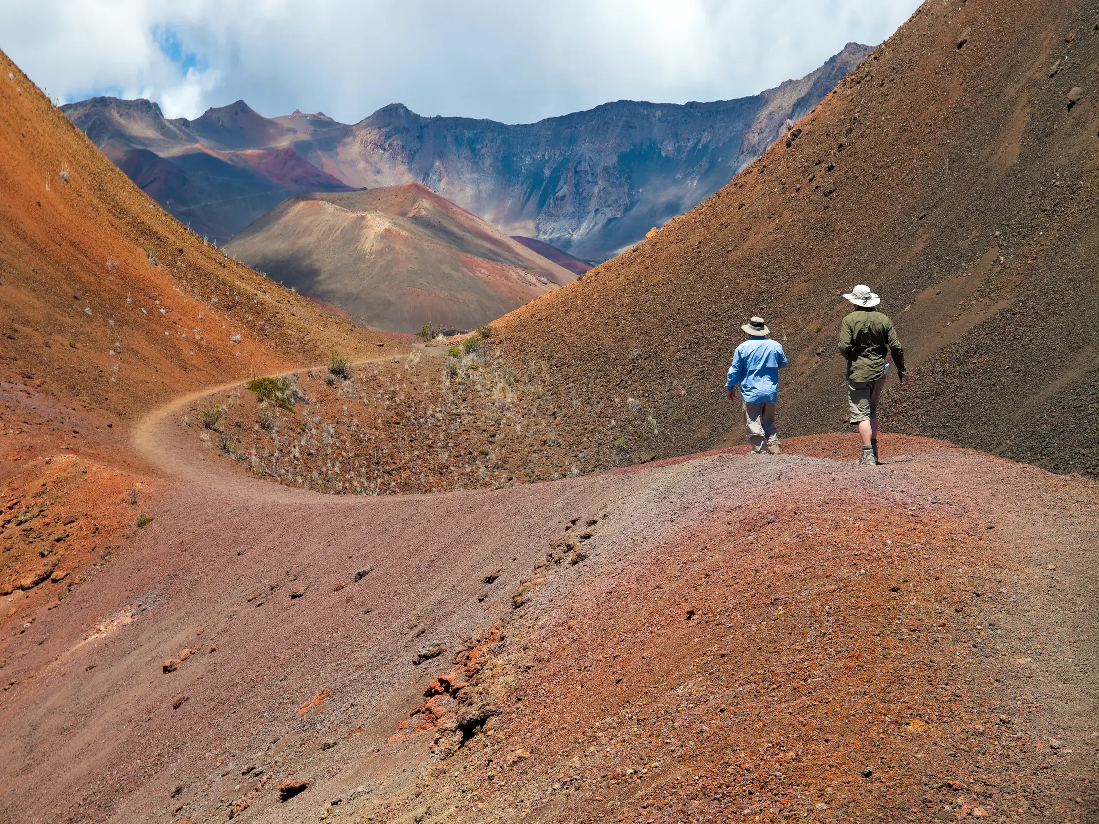 Zwei Personen wandern auf einer Studienreise über einen Pfad in der roten Vulkanlandschaft des Haleakala-Nationalparks auf Maui.