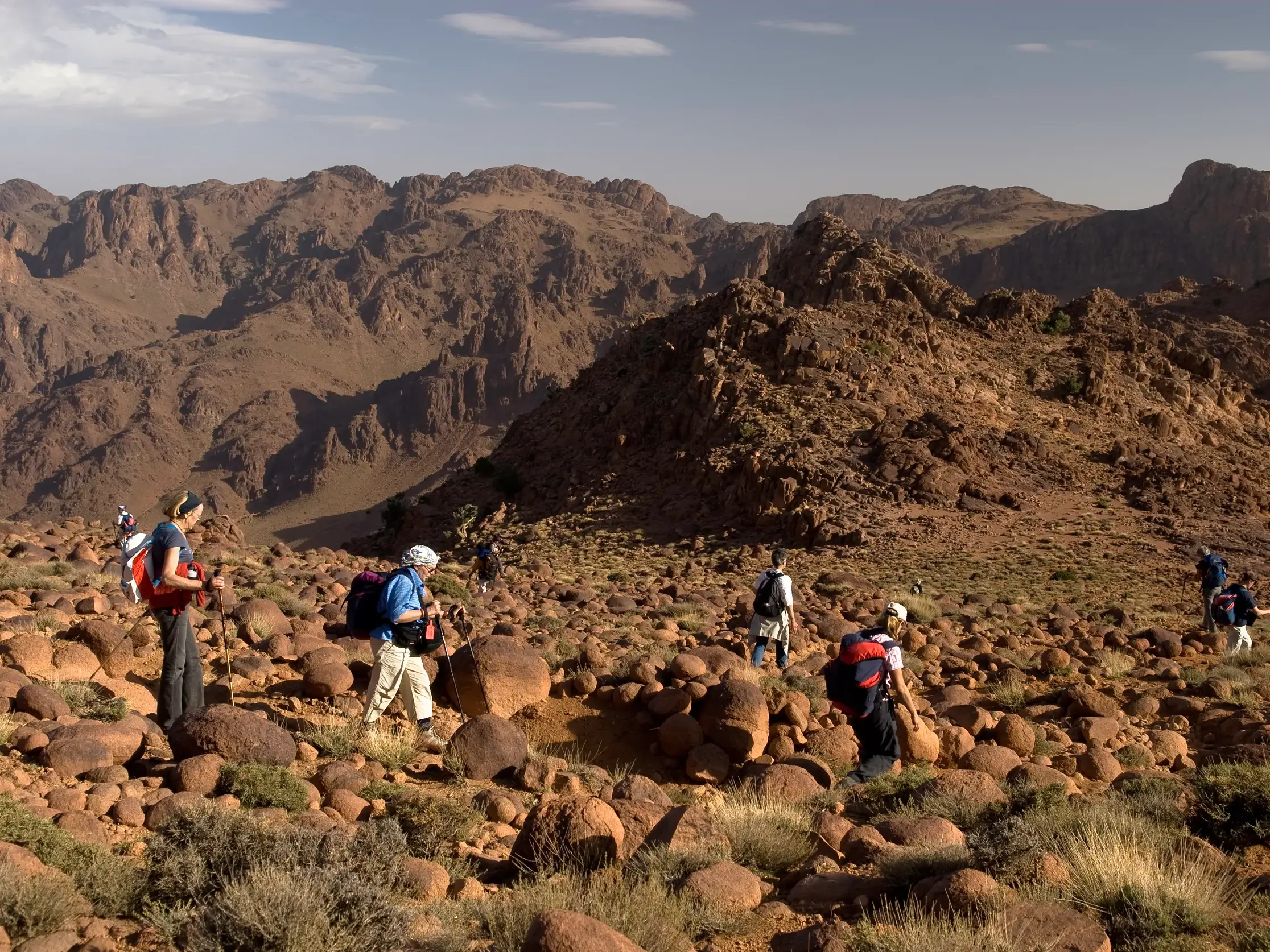 Eine Wandergruppe mit Rucksäcken und Stöcken beim Trekking durch die weite, steinige Landschaft des Saghro-Gebirges in Marokko.