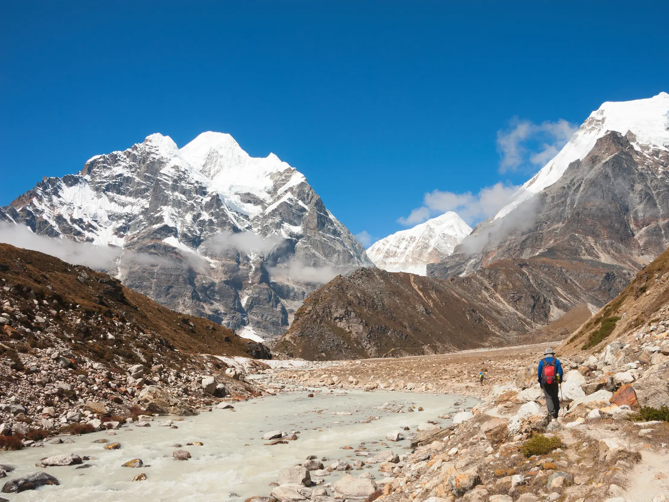 Ein Wanderer folgt dem Pfad durch das weite, steinige Barun-Tal in Nepal, im Hintergrund ragen eisige Himalaya-Gipfel auf.
