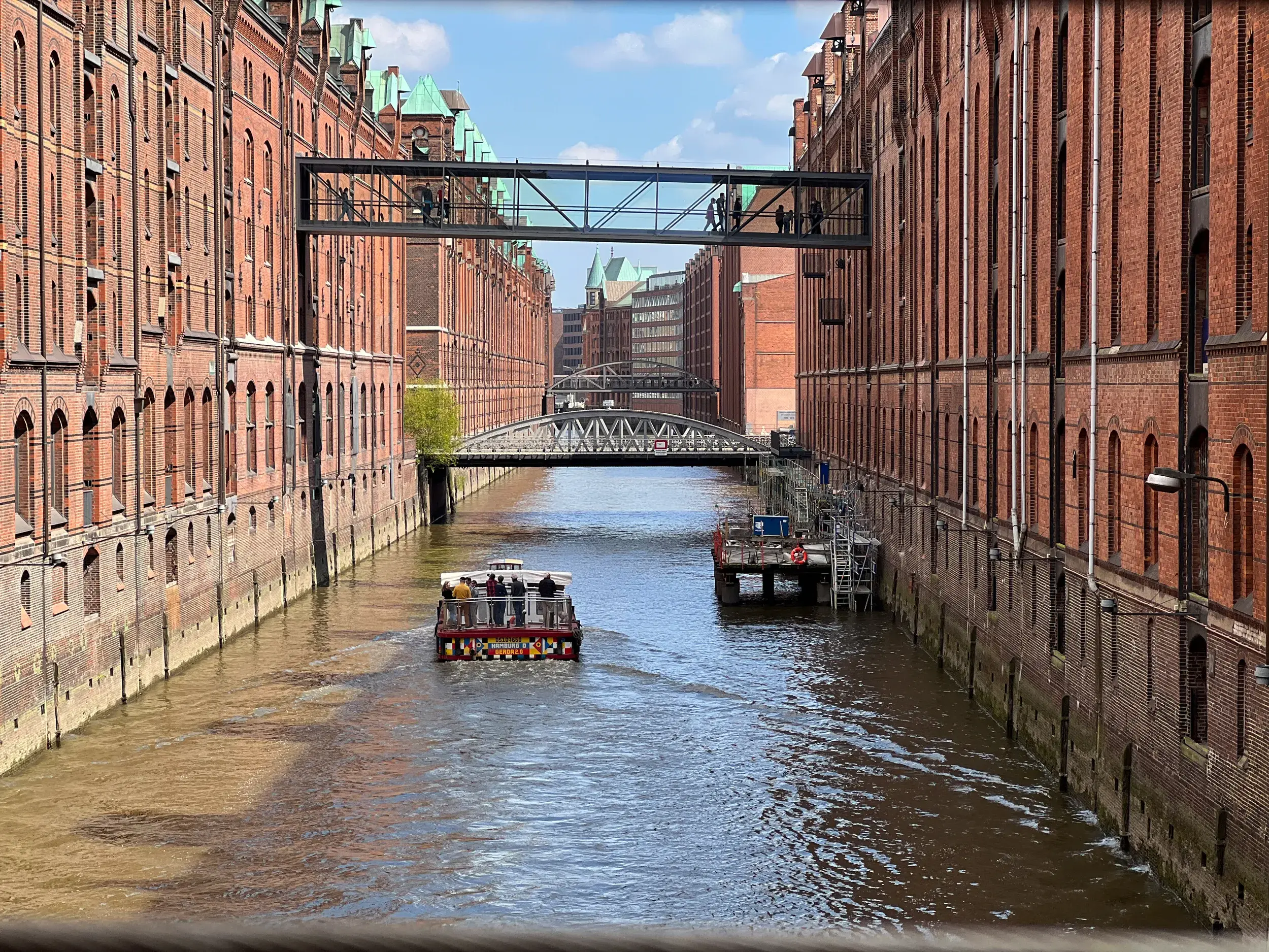 Barkasse bei einer Hafenrundfahrt auf einem Fleet zwischen Backsteinbauten der Speicherstadt in Hamburg