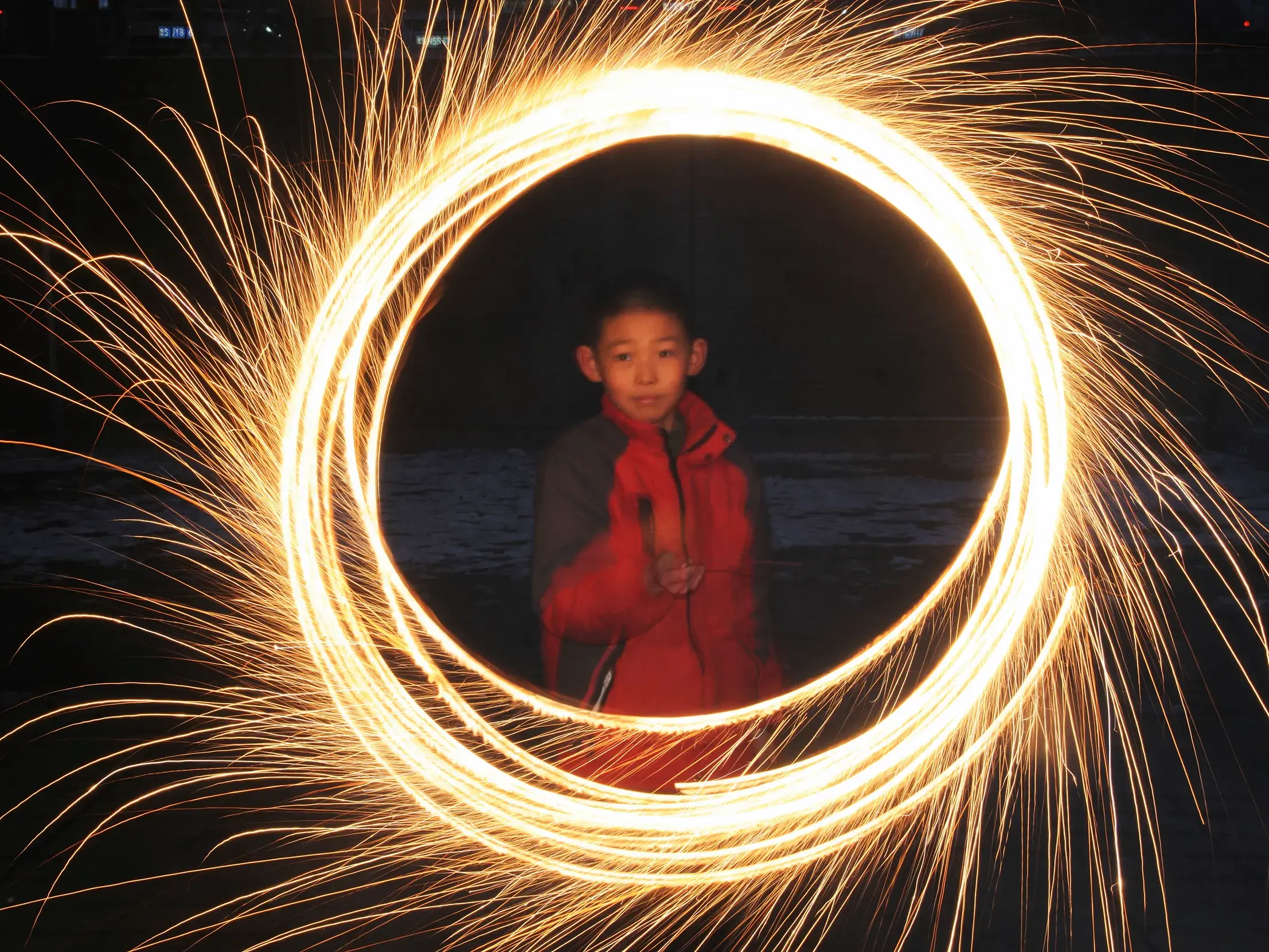 Langzeitbelichtung bei Nacht: Ein chinesischer Junge malt mit rotierenden Funken einen magischen Lichtkreis in die Luft.