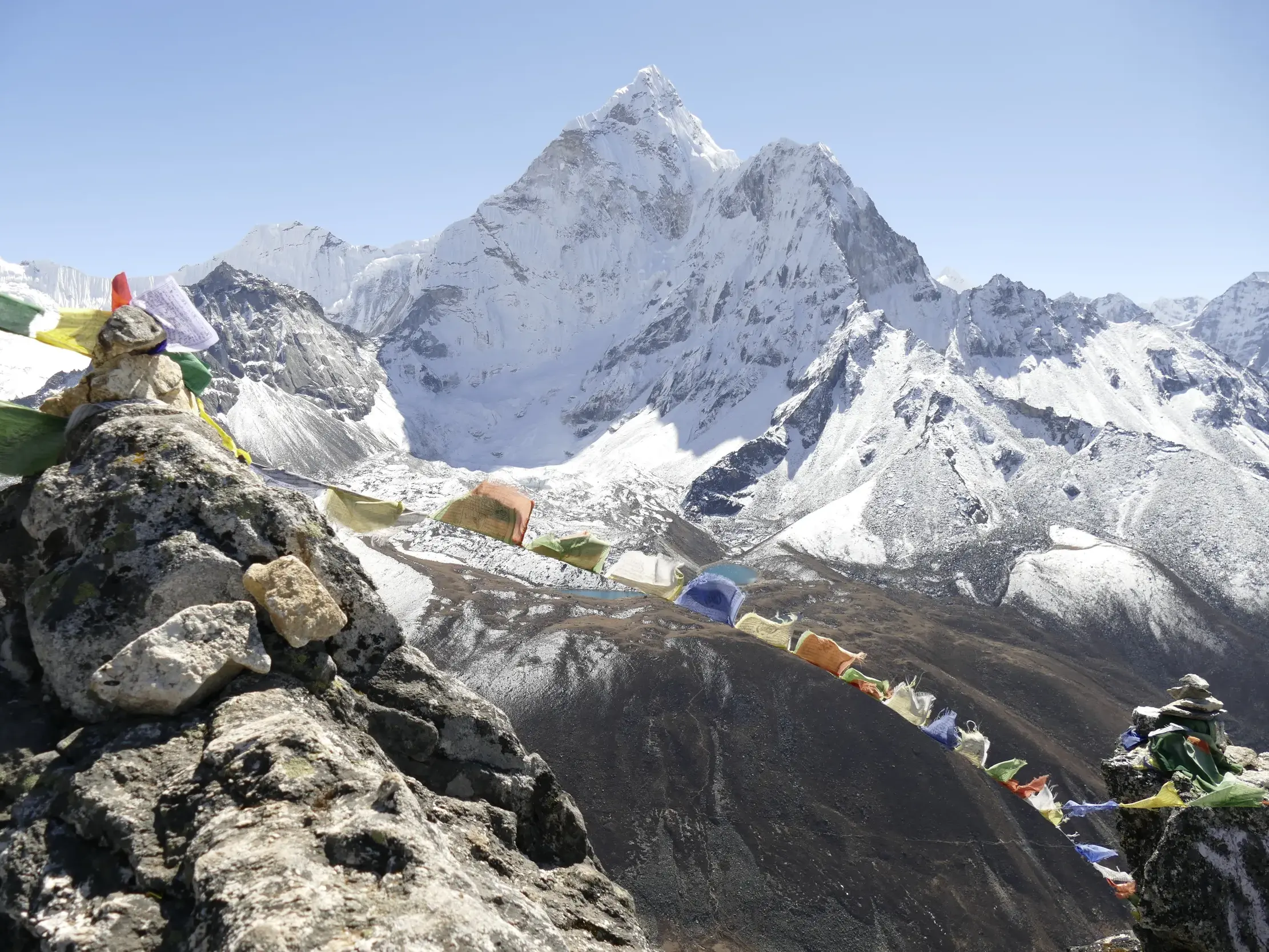 Bunte Gebetsfahnen wehen im Wind an einem Steinmännchen vor dem schneebedeckten Gipfel des Ama Dablam im Himalaya in Nepal.
