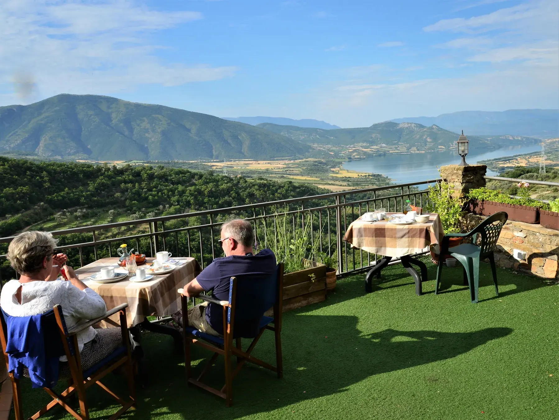 Paar genießt Frühstück auf der Terrasse eines Gästehauses mit Blick auf einen See in der Berglandschaft der südlichen Pyrenäen.