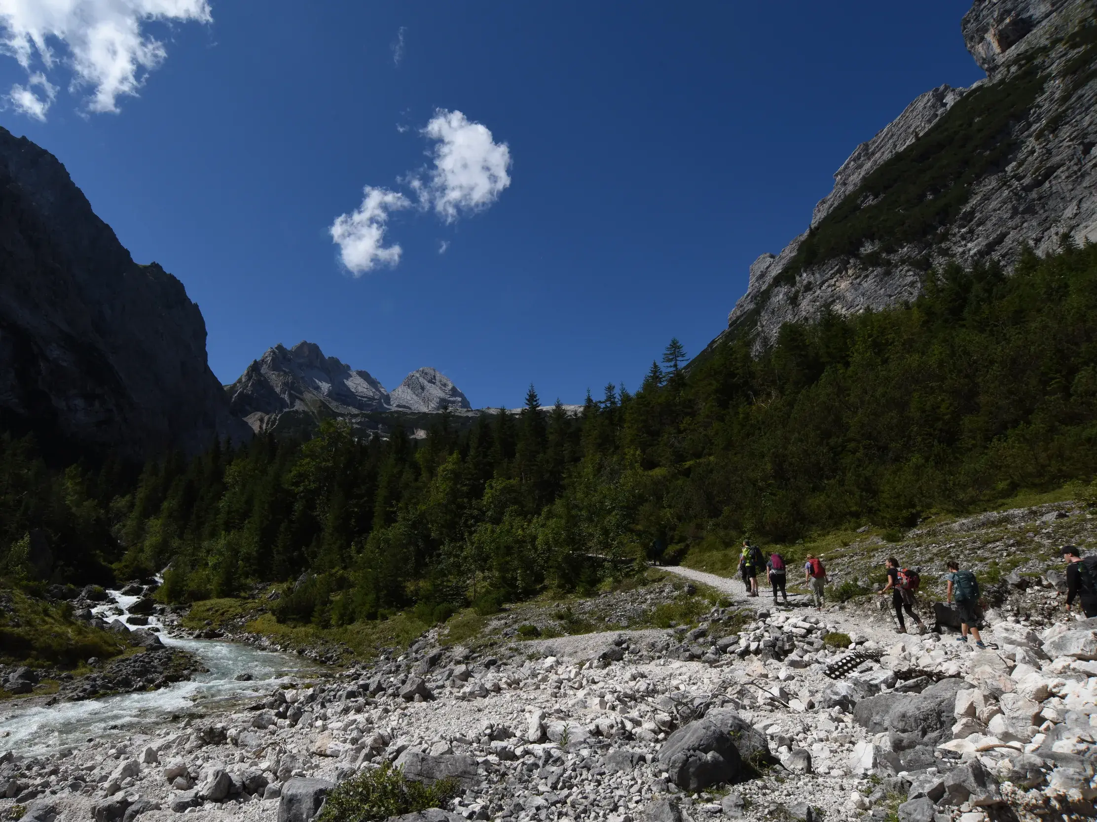 Eine Trekkinggruppe wandert auf einem steinigen Pfad durch das idyllische Reintal, begleitet von der rauschenden Partnach.