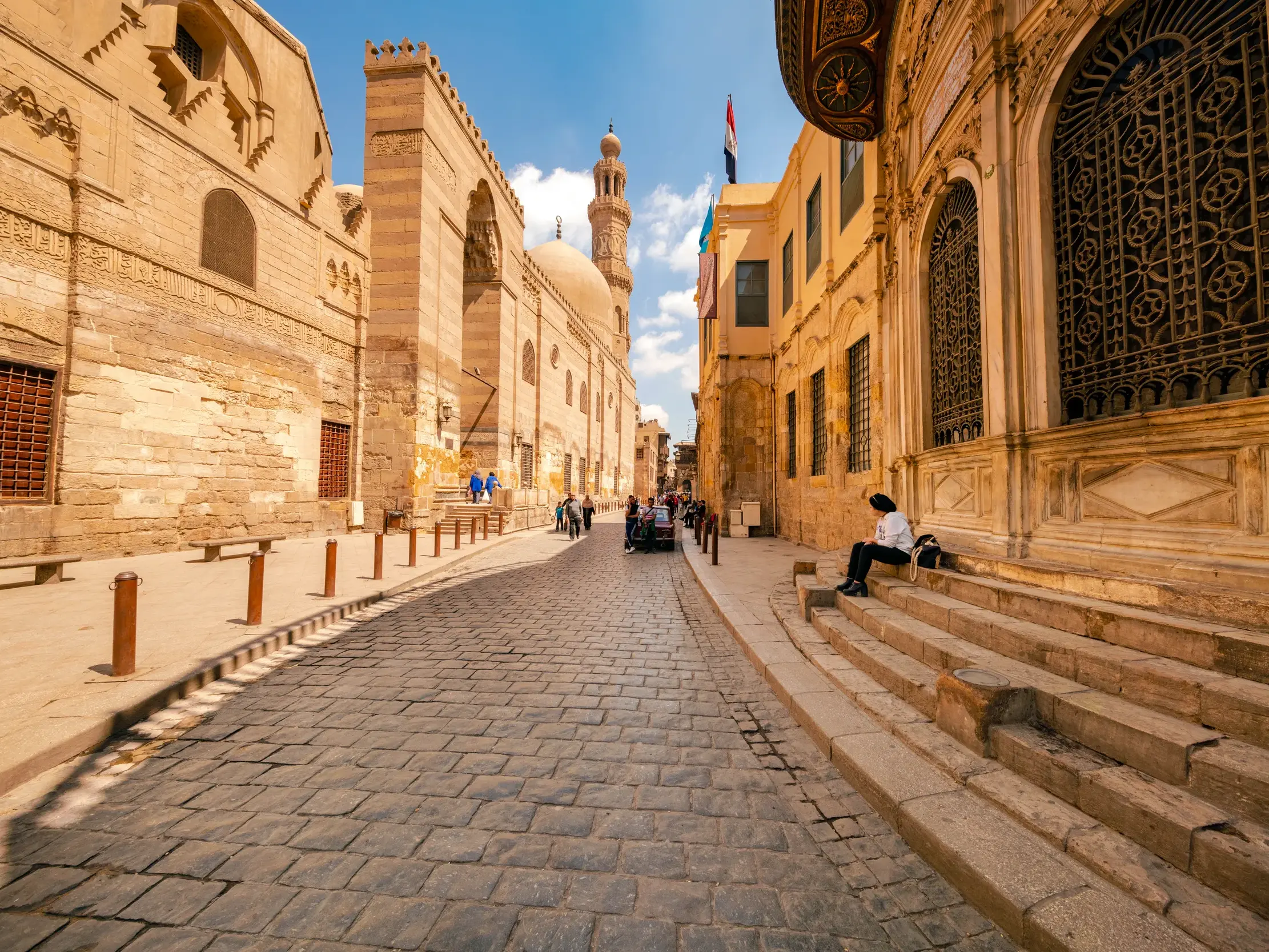 Gepflasterte Gasse in der Altstadt von Kairo, vorbei am Grabkomplex al-Mansur Qalawun unter blauem Himmel bei Sonnenschein.