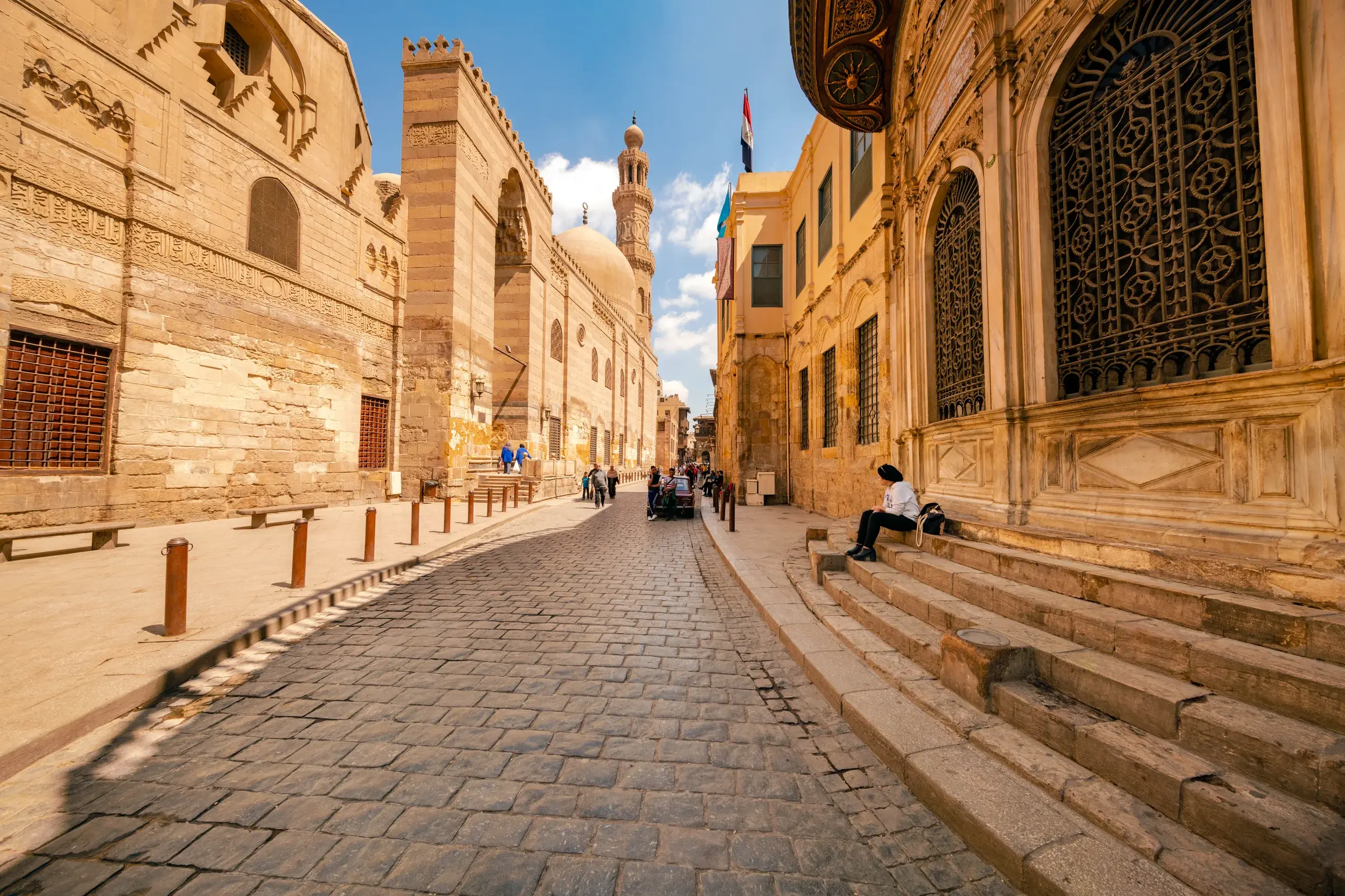 Gepflasterte Gasse in der Altstadt von Kairo, vorbei am Grabkomplex al-Mansur Qalawun unter blauem Himmel bei Sonnenschein.