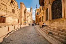 Gepflasterte Gasse in der Altstadt von Kairo, vorbei am Grabkomplex al-Mansur Qalawun unter blauem Himmel bei Sonnenschein.