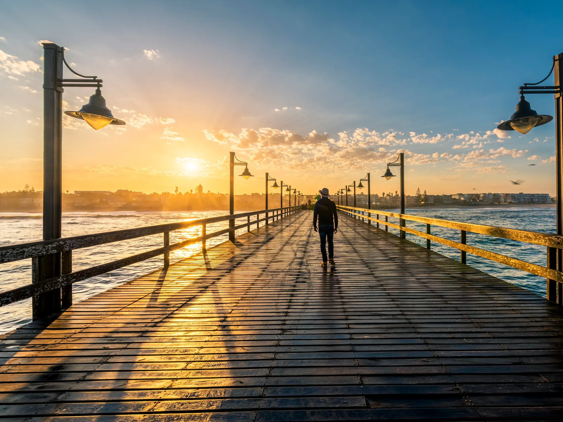 Ein Reisender spaziert bei Sonnenuntergang auf der historischen Seebrücke von Swakopmund, Namibia, in die goldene Abendsonne.