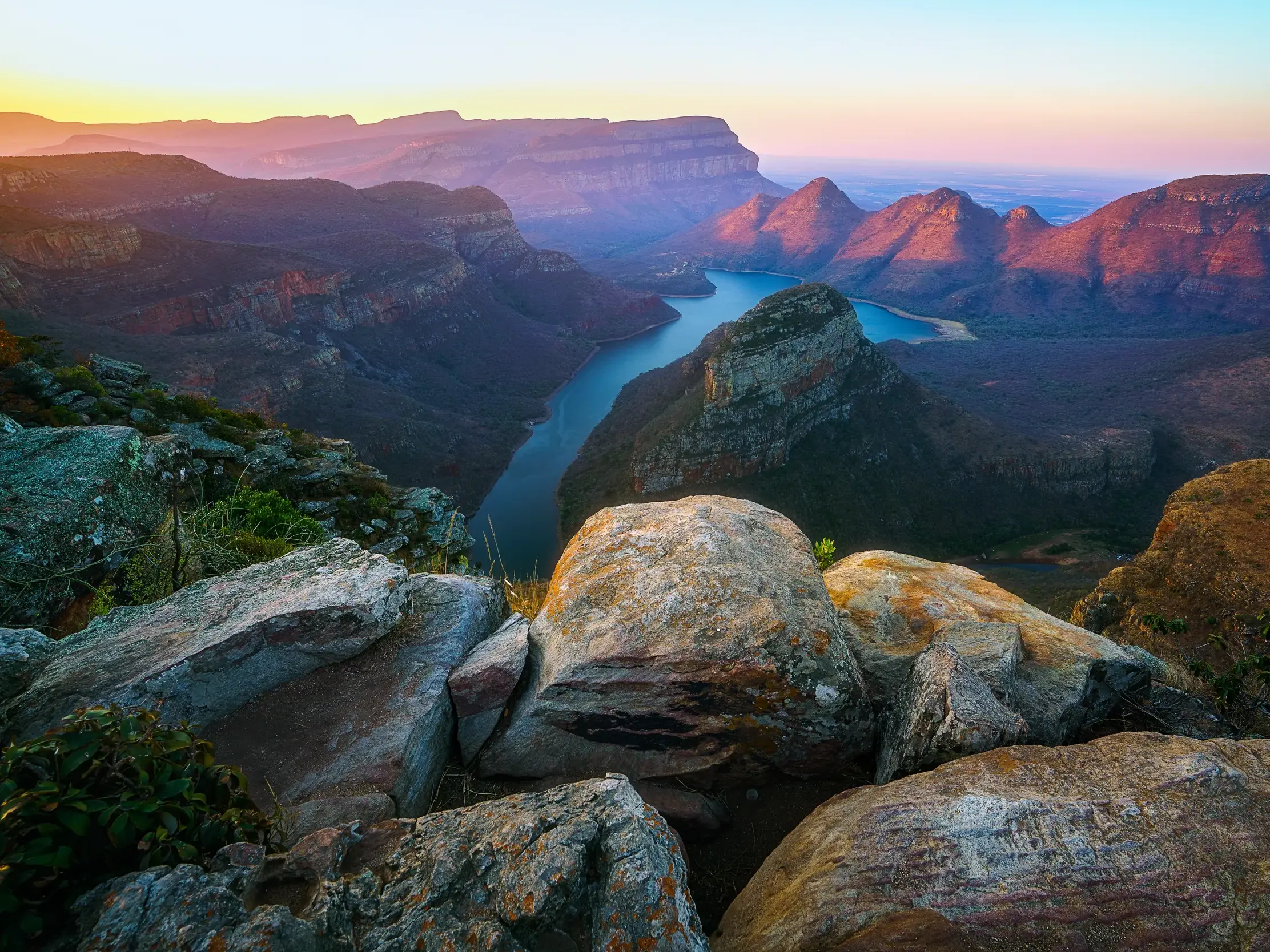 Goldene Morgensonne über dem Blyde River Canyon in Südafrika, mit Blick von Felsen auf den Fluss und die Three Rondavels.
