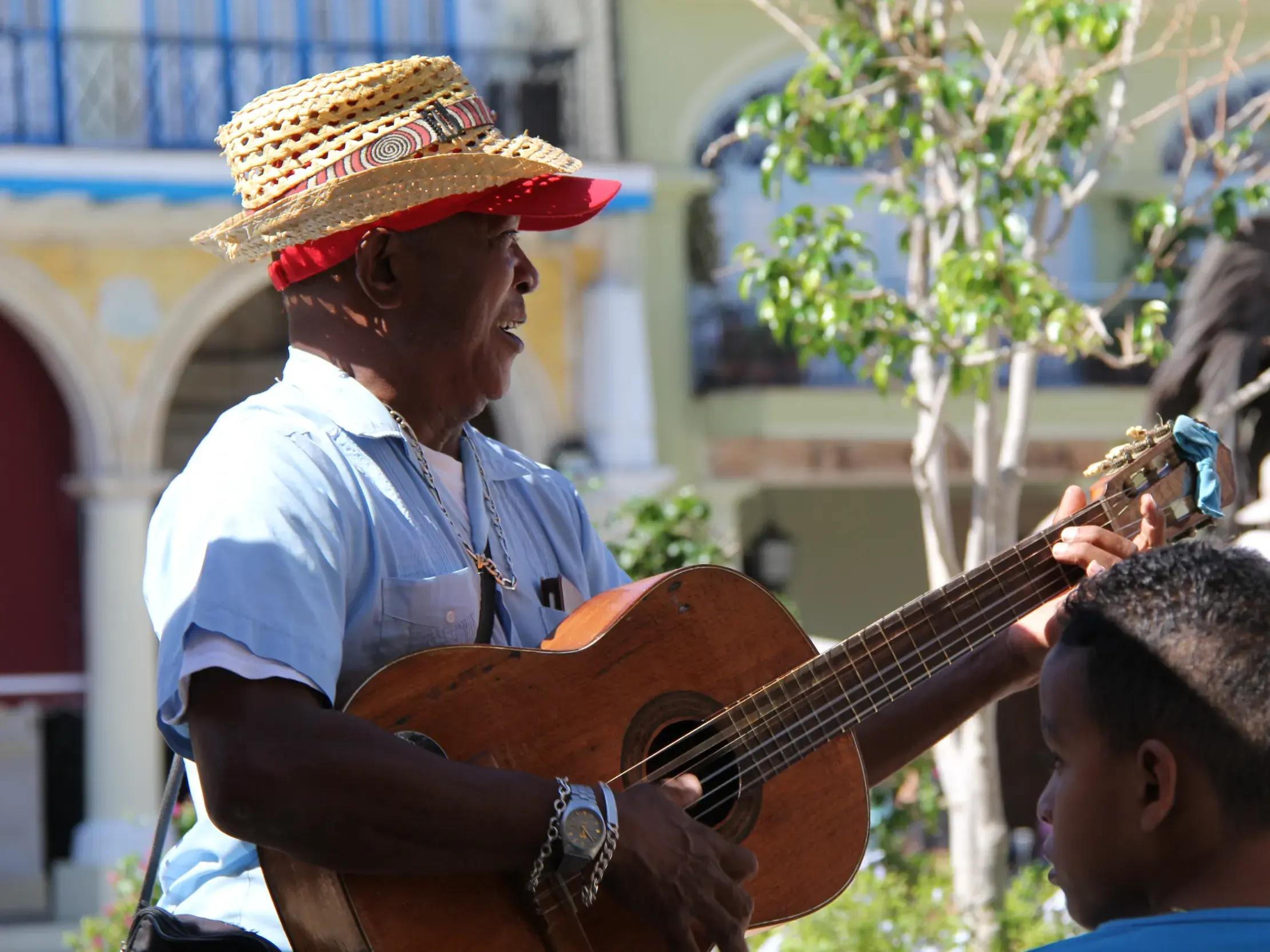 Kubanischer Straßenmusiker mit Strohhut singt und spielt Gitarre für einen Jungen in den belebten Gassen Havannas.