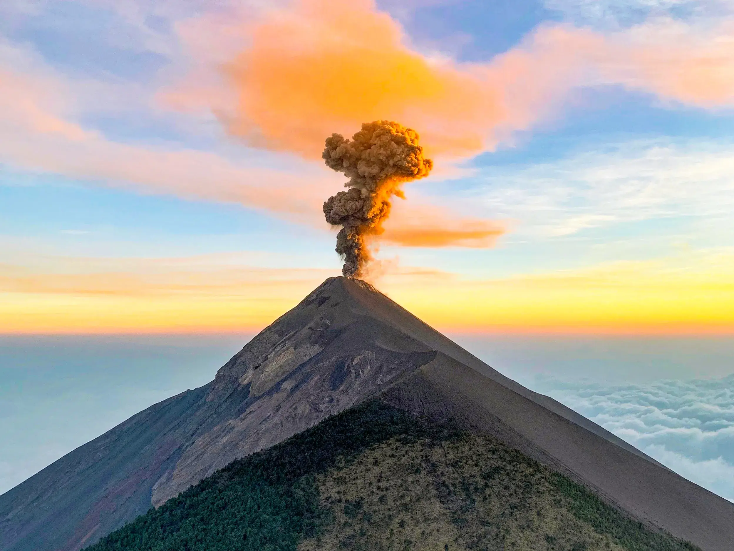 Eruption des Vulkans Fuego in Guatemala bei Sonnenuntergang, gesehen vom Gipfel des Acatenango über einem Wolkenmeer.
