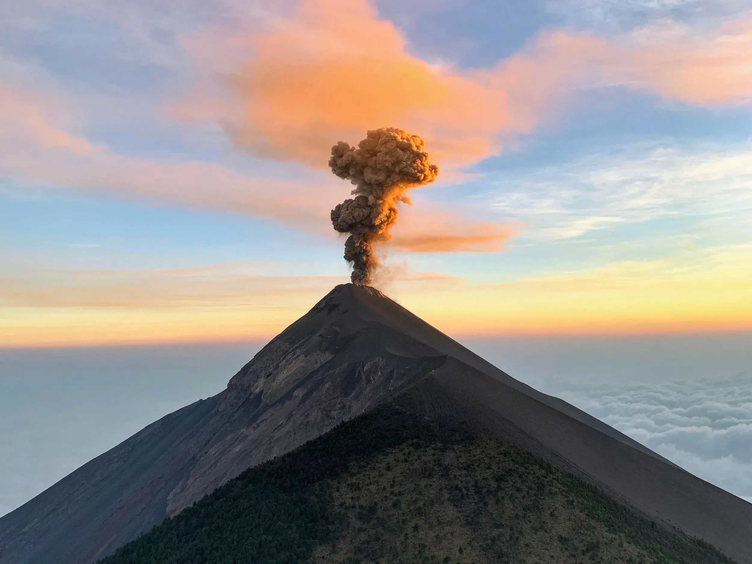 Eruption des Vulkans Fuego in Guatemala bei Sonnenuntergang, gesehen vom Gipfel des Acatenango über einem Wolkenmeer.