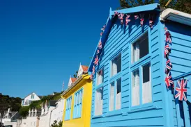 Bunte, mit britischen Flaggen geschmückte Holzhäuser an einem sonnigen Tag in einem Küstenort auf Jersey.