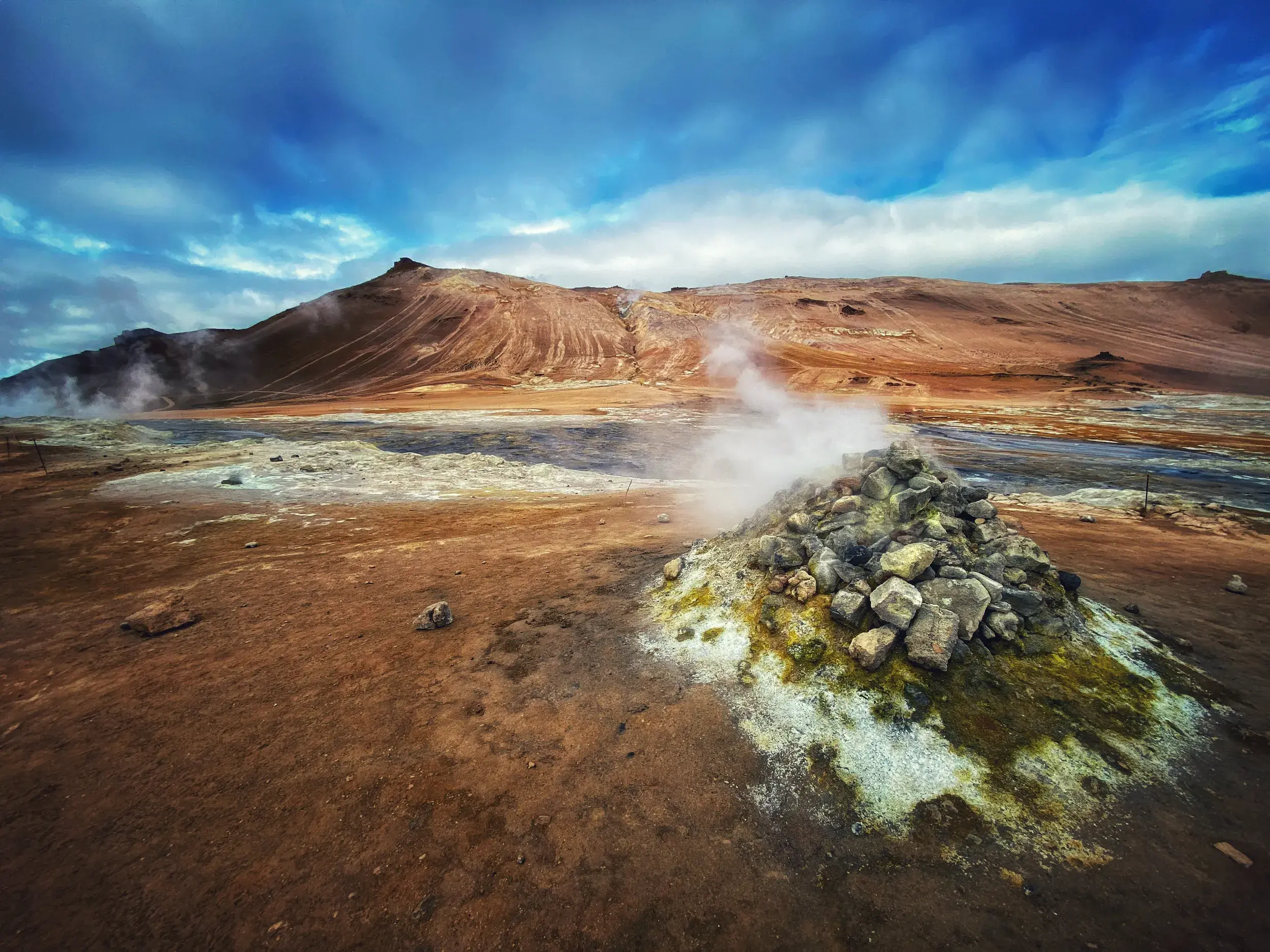Eine dampfende Fumarole mit Schwefelablagerungen in der kargen Vulkanlandschaft des Geothermalgebiets Hverarönd in Island.