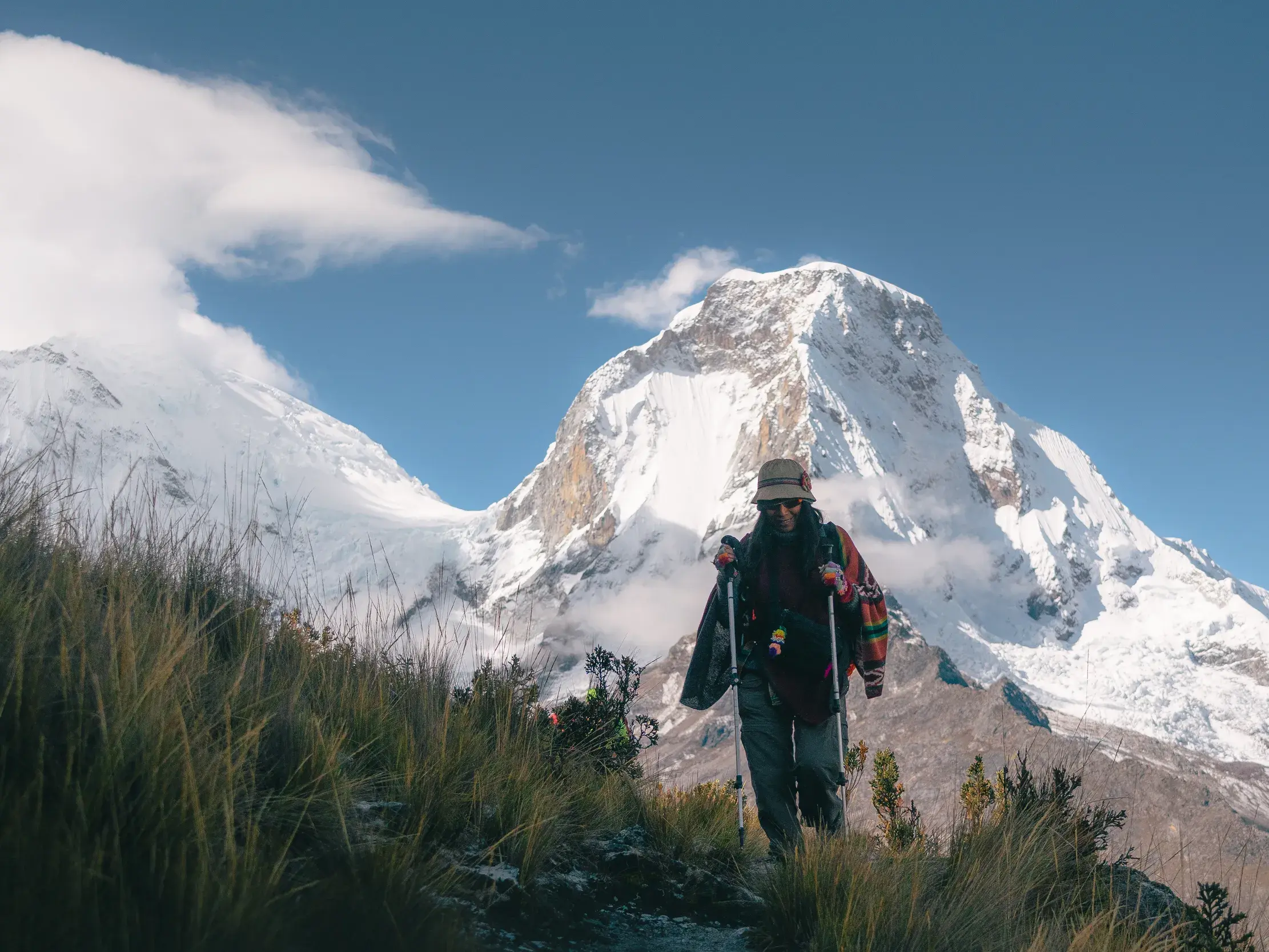 Eine Wanderin mit Trekkingstöcken und Rucksack auf einem schmalen Pfad in der Berglandschaft der Cordillera Blanca in Peru.