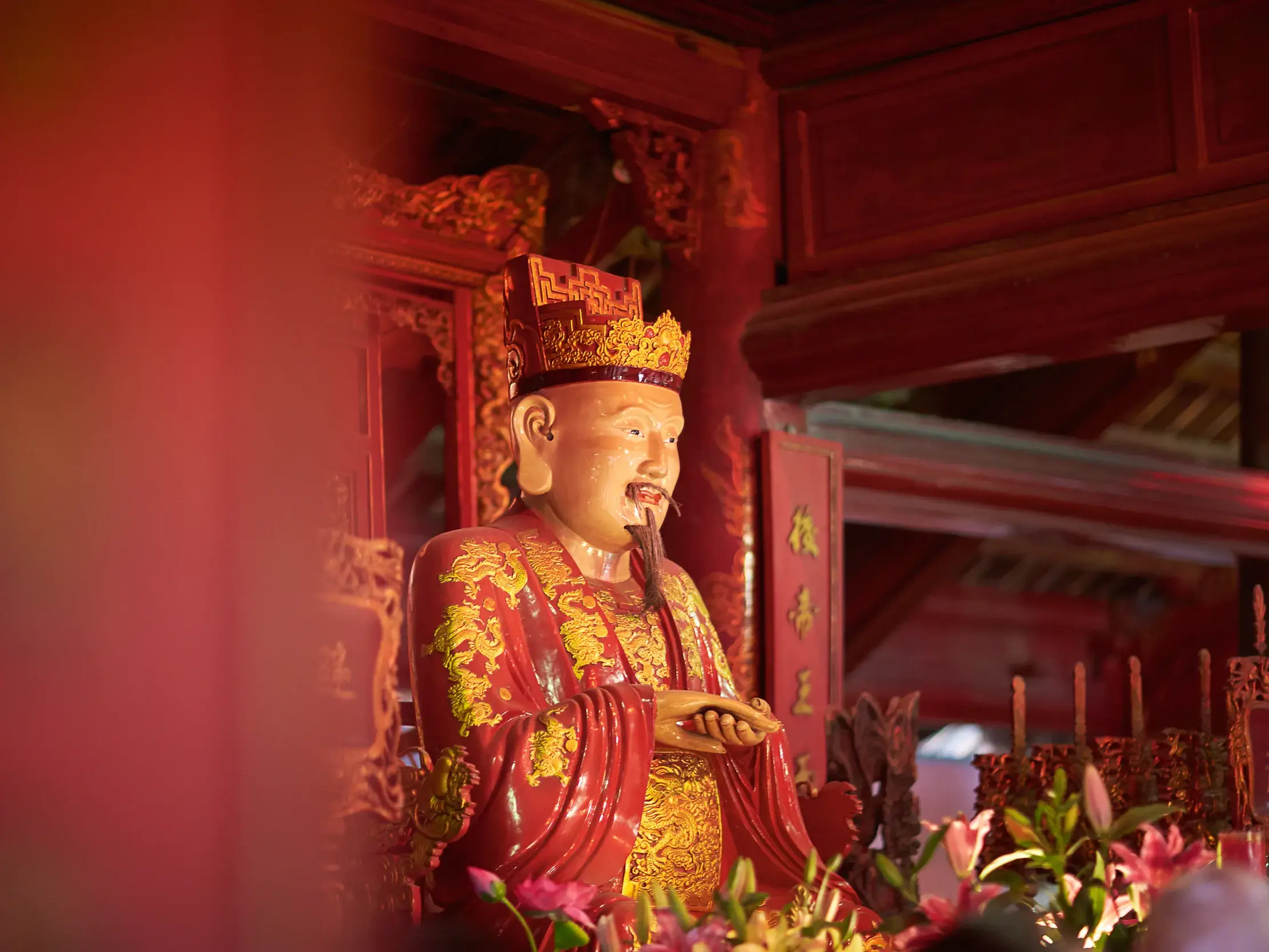 Rote Statue eines Gelehrten mit Krone und Bart im berühmten Literaturtempel in Hanoi, Vietnam.