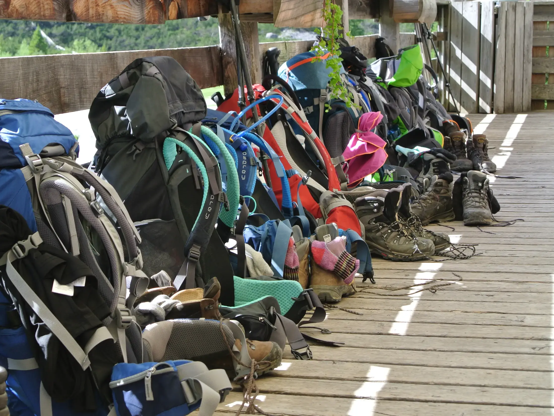 Aufgereihte Trekkingrucksäcke und Wanderschuhe einer Gruppe auf der Holzterrasse einer Berghütte in den Sextner Dolomiten.