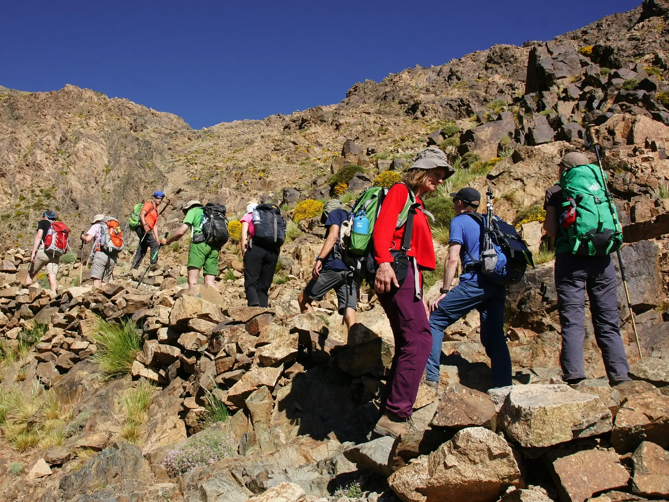 Eine Hauser-Reisegruppe beim anspruchsvollen Trekking auf einem steinigen Bergpfad im sonnigen Hohen Atlas in Marokko.