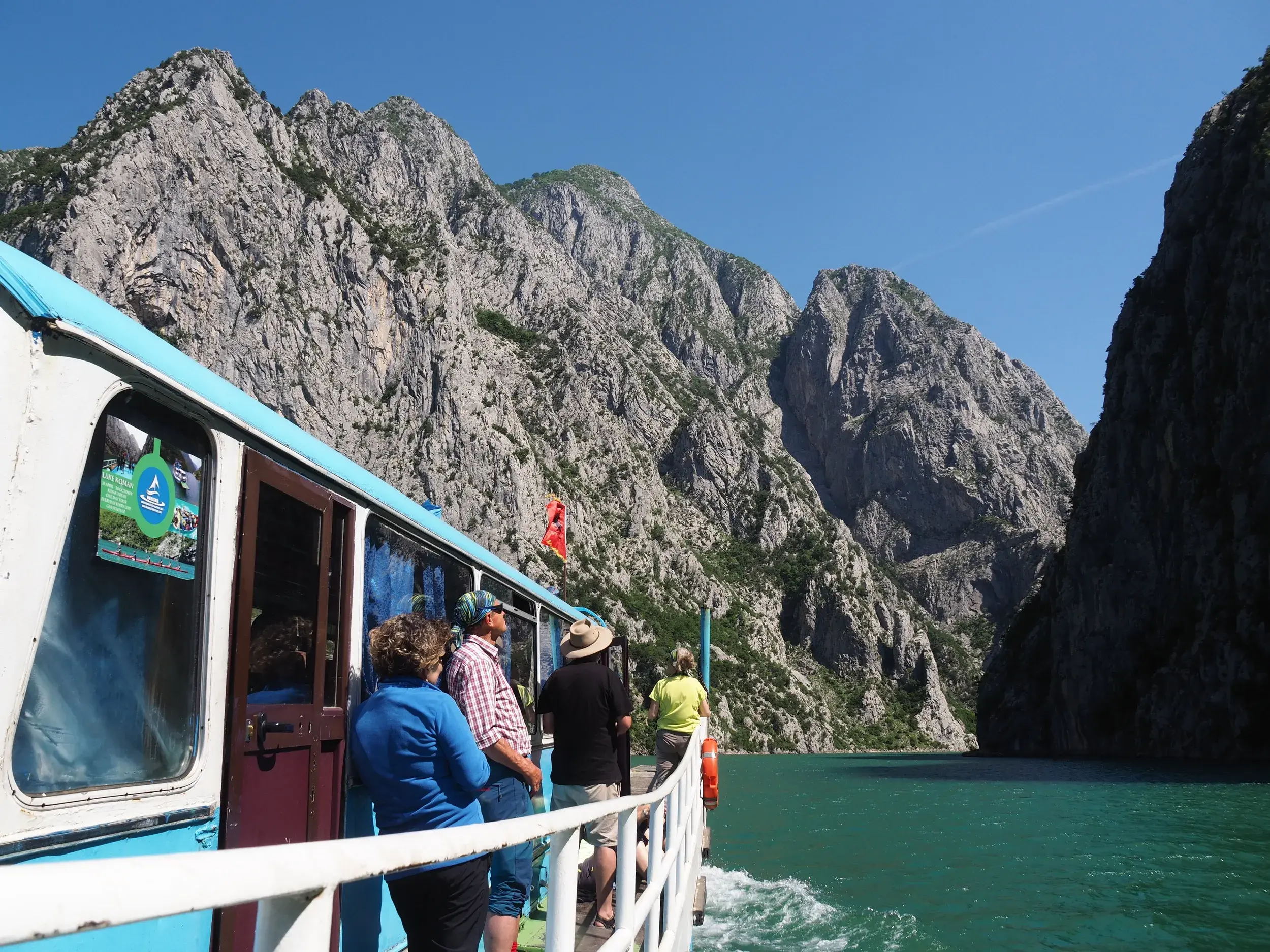 Eine Reisegruppe genießt die sonnige Fährfahrt auf dem türkisen Koman-Stausee durch die steilen Felswände der Drin-Schlucht.