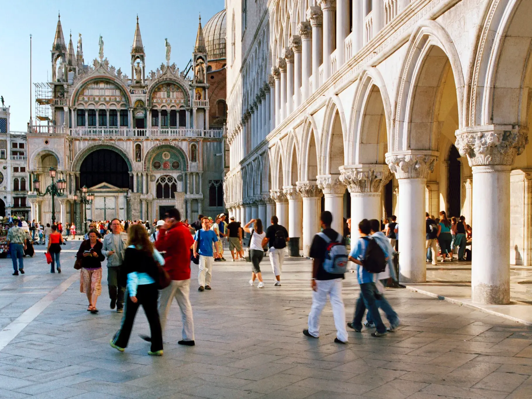 Besucher flanieren am Nachmittag über den Markusplatz in Venedig mit Blick auf den prachtvollen Markusdom und den Dogenpalast.
