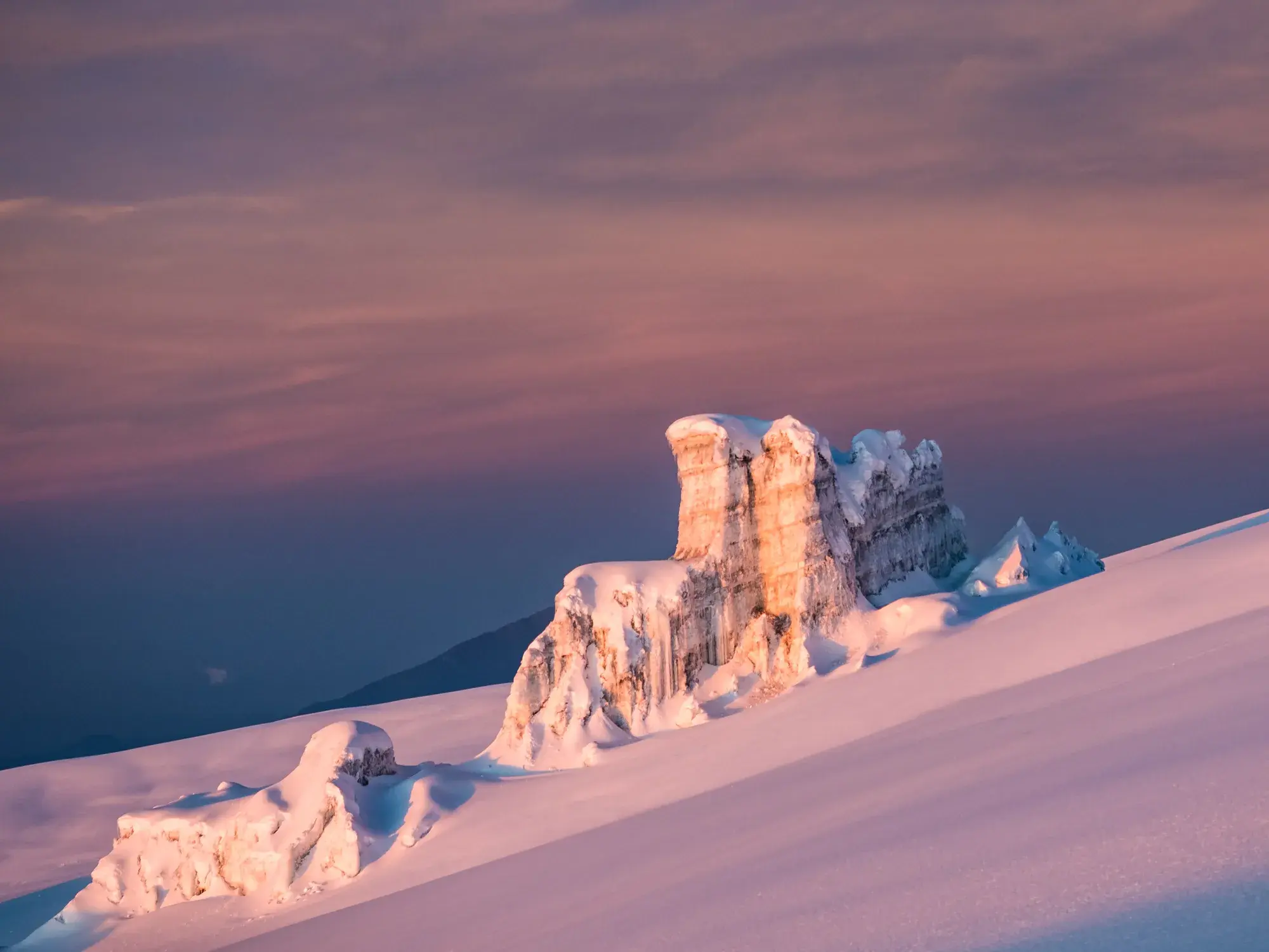 Schneebedeckte Gletscherformationen am Kraterrand des Kilimanjaro, angestrahlt vom rosa Licht des Sonnenaufgangs.