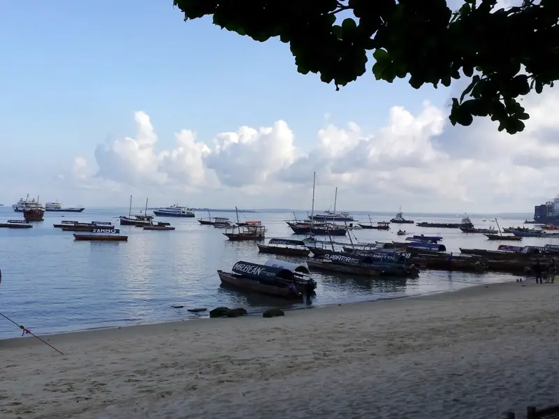 Viele traditionelle Dhaus und Boote ankern im Indischen Ozean vor einem Sandstrand in Stone Town auf Sansibar.