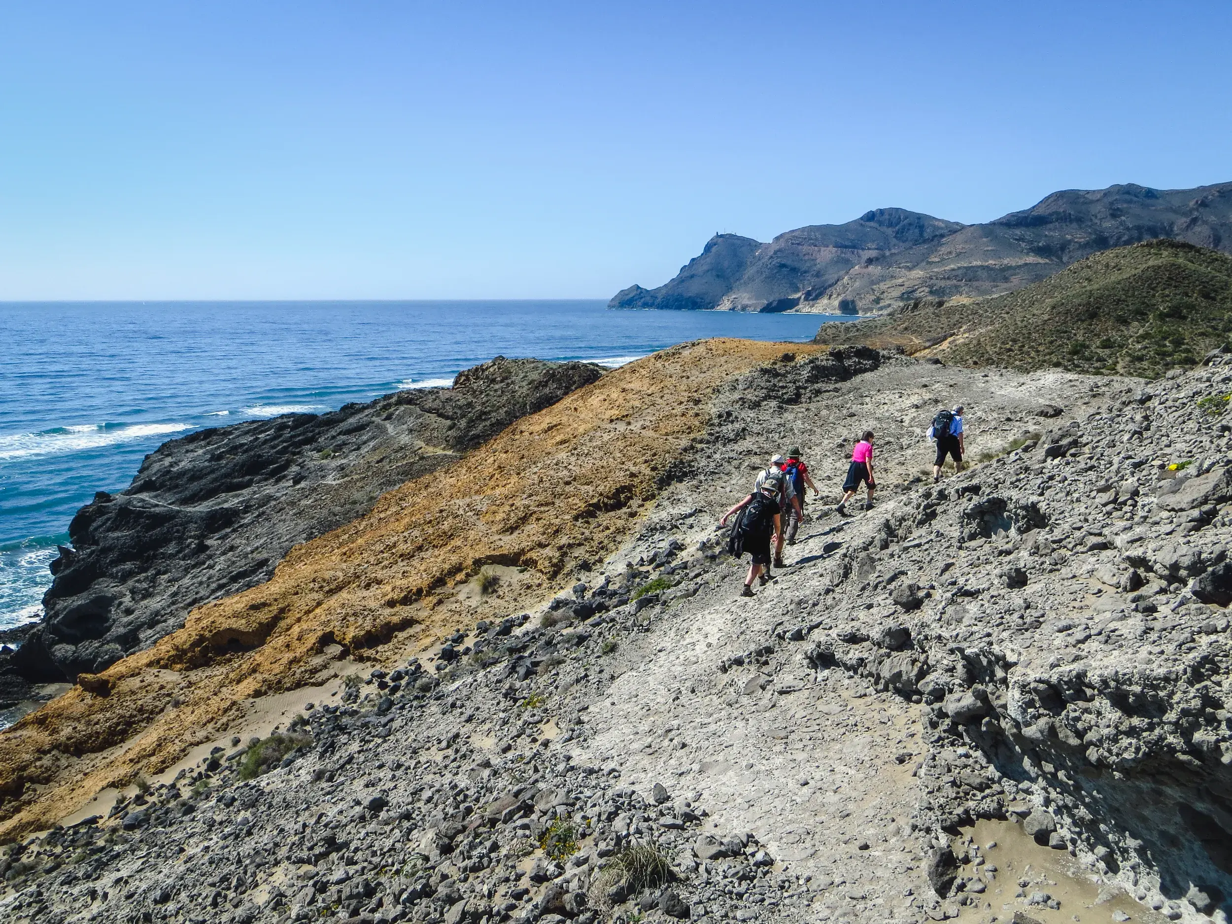 Eine kleine Wandergruppe wandert auf einem steinigen Pfad an der Steilküste des Naturparks Cabo de Gata in Andalusien.