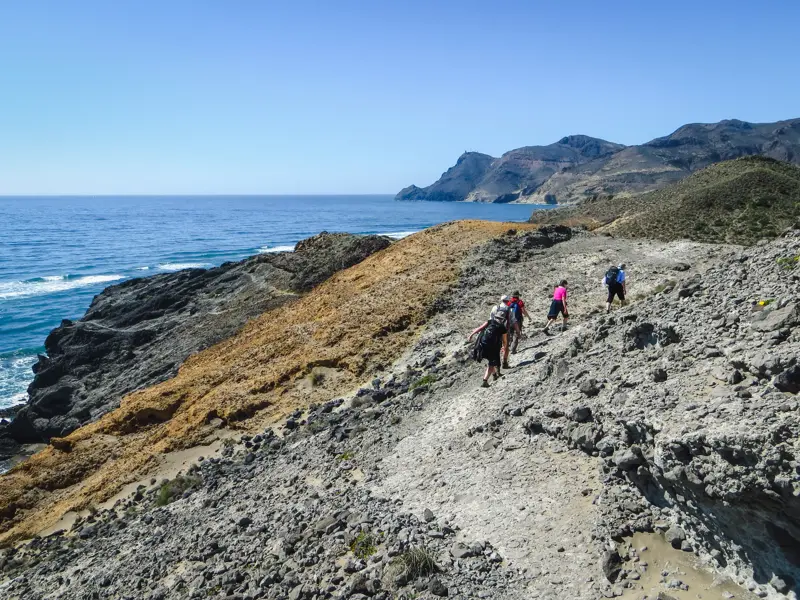 Eine kleine Wandergruppe wandert auf einem steinigen Pfad an der Steilküste des Naturparks Cabo de Gata in Andalusien.