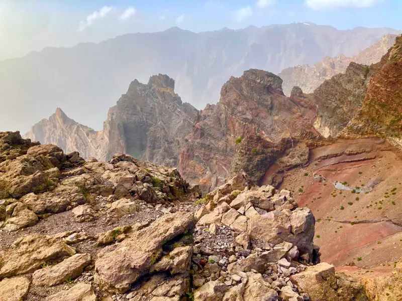 Ein schmaler Wanderweg führt durch eine karge, felsige Vulkanlandschaft mit Blick in die Caldera de Taburiente auf La Palma.